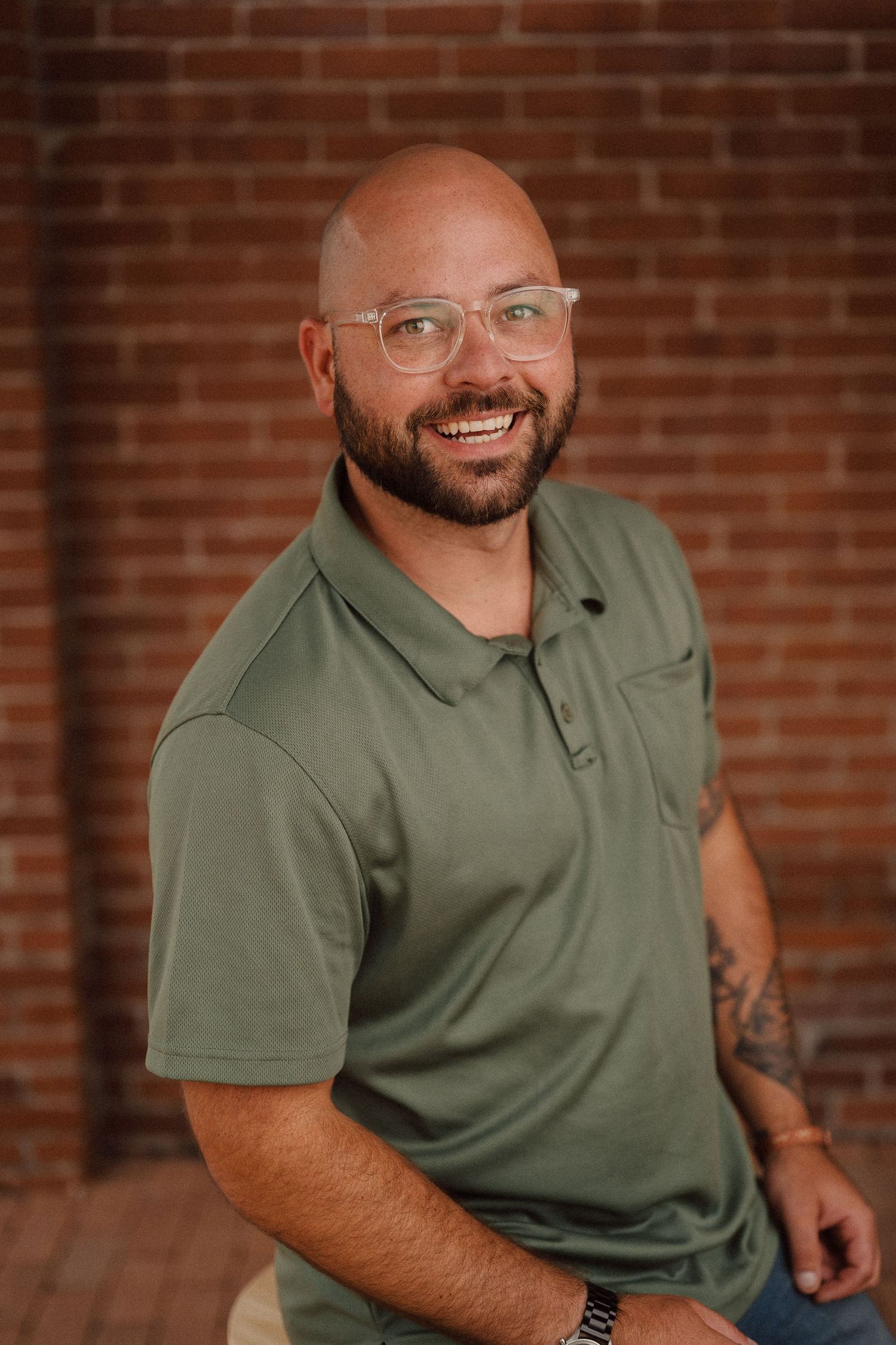 Casual professional portrait of a person in green polo shirt smiling against red brick background.