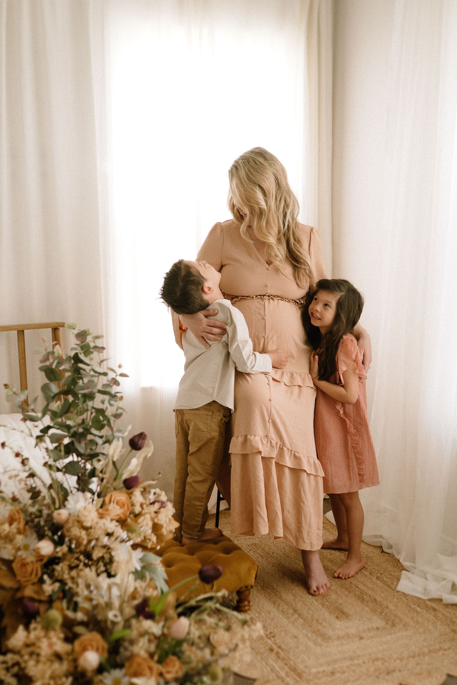 Candid family moments captured in soft natural light with coordinating peach and neutral outfits against white walls.