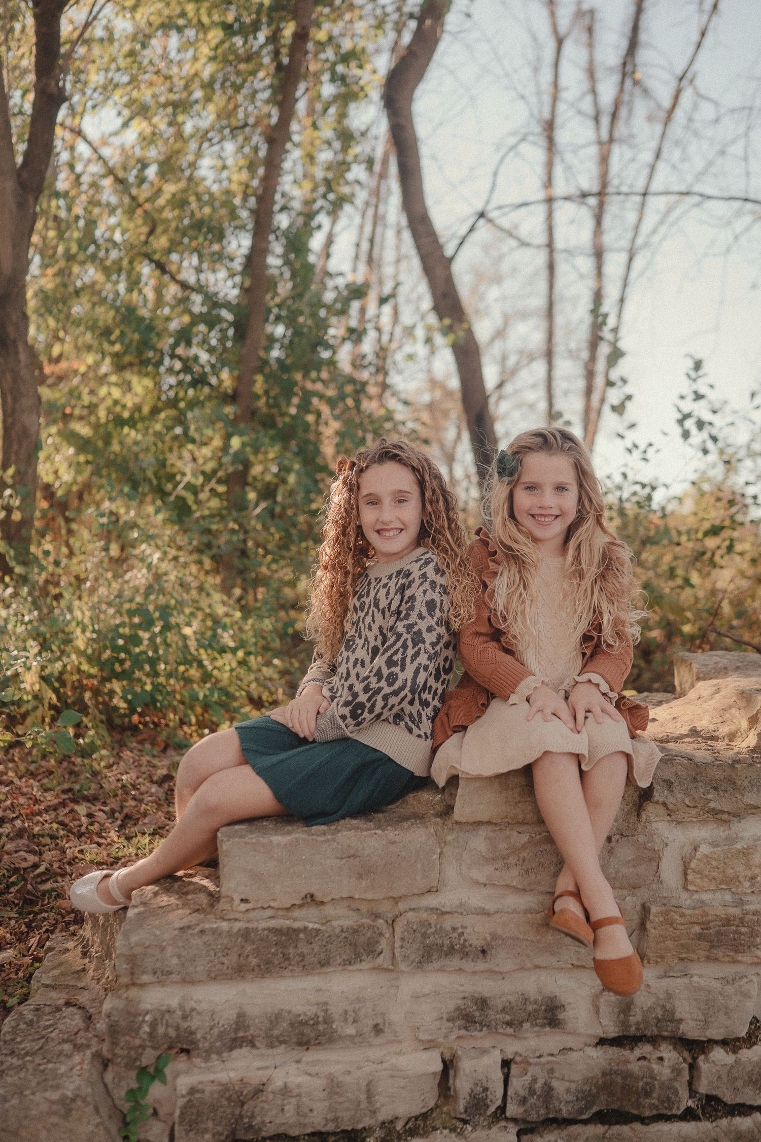 Two people lounging on stone wall in coordinated fall outfits during outdoor autumn photoshoot.