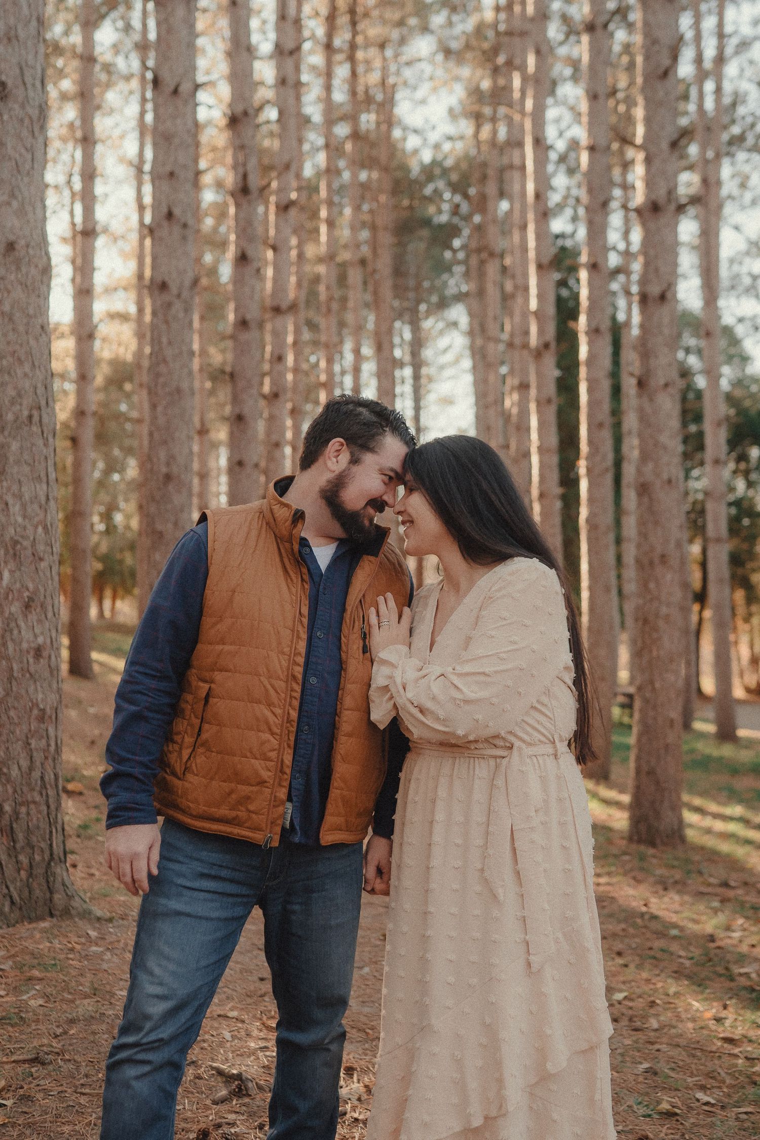 A couple shares romantic moments among tall pine trees during a sunset photo session in the woods.