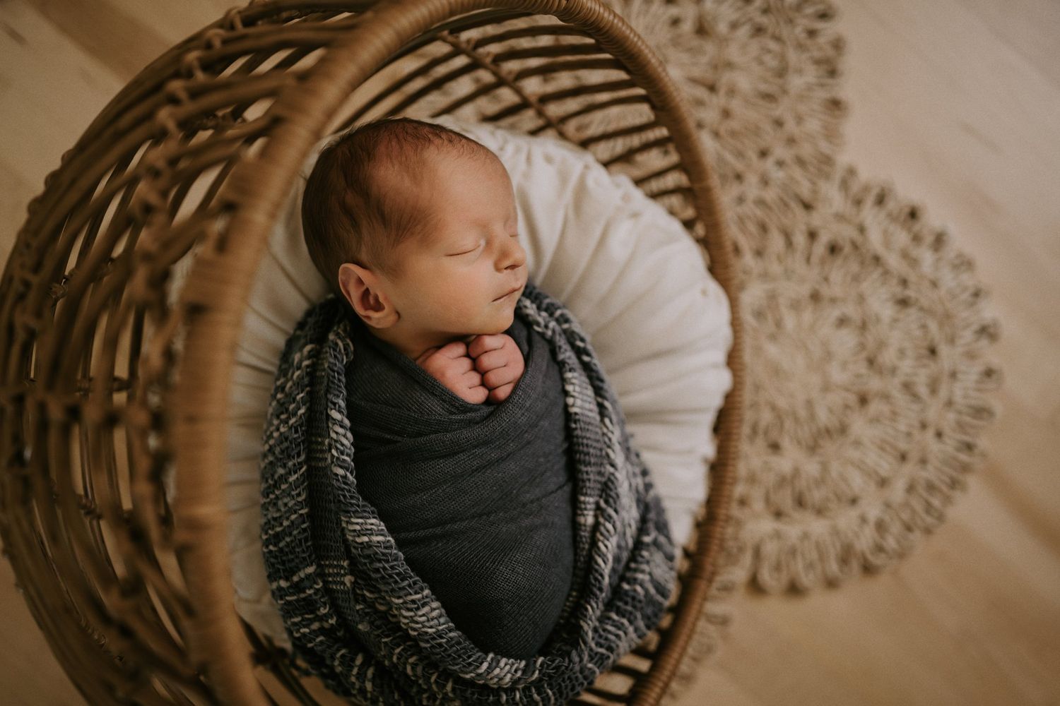 A newborn baby wrapped in dark fabric sleeping peacefully in a woven basket.