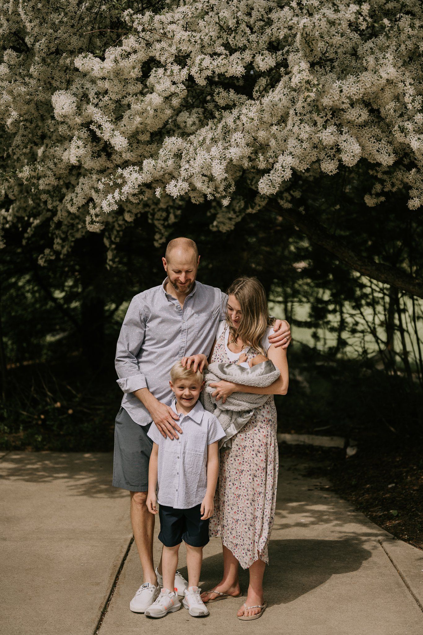 Family standing together beneath blooming spring trees on a sunny day.