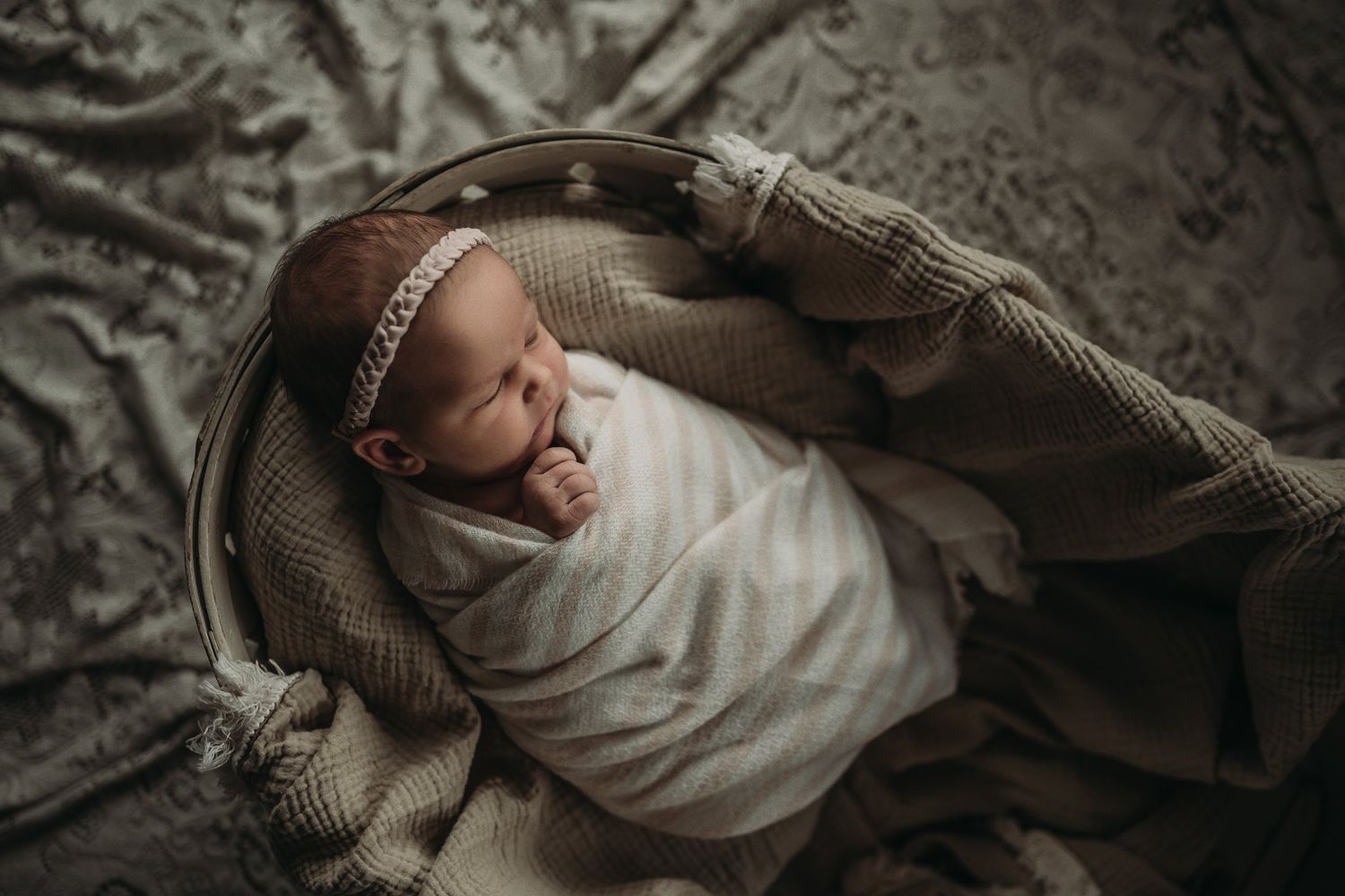 Overhead view of peaceful infant swaddled in white with knit blanket and lace backdrop.