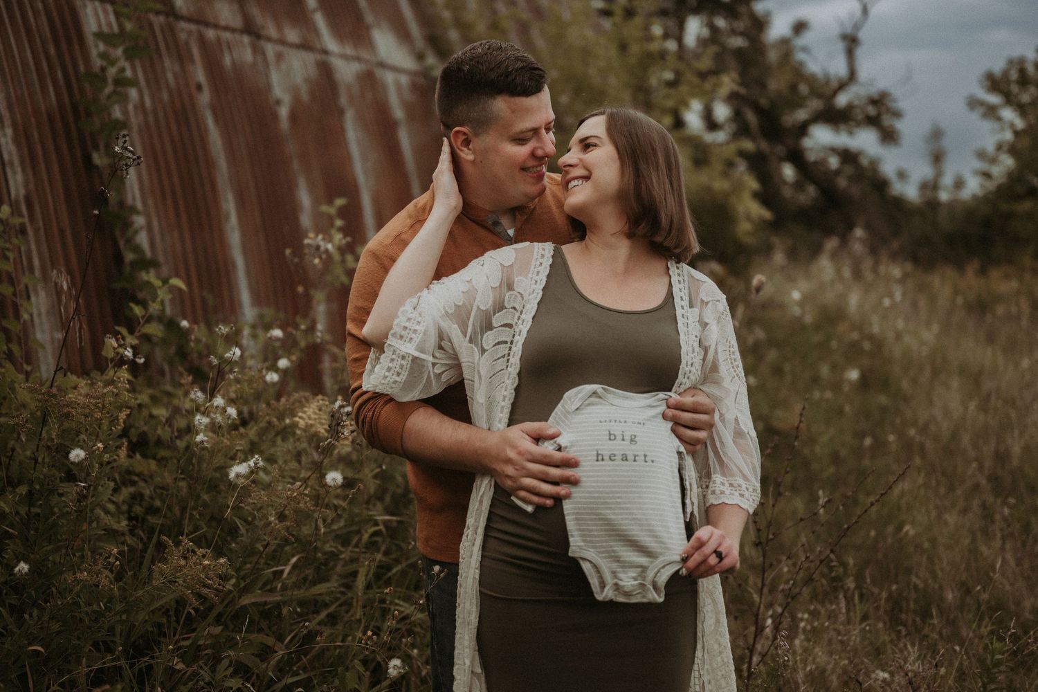 A maternity photo session featuring a couple holding a onesie with text.
