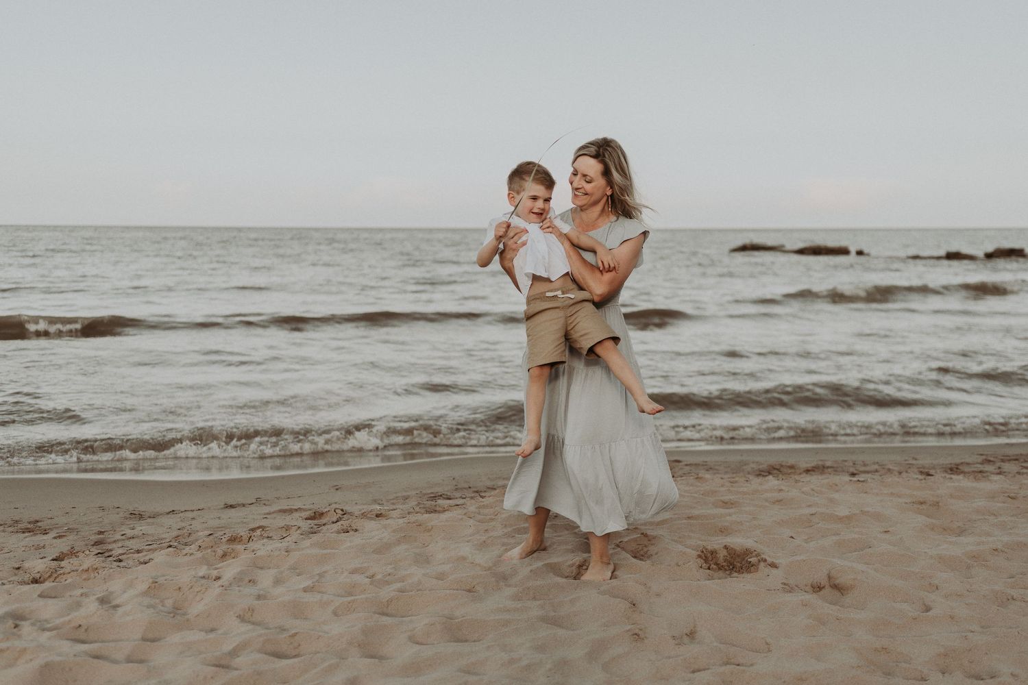Two people embrace while standing on a cloudy beach near the ocean.