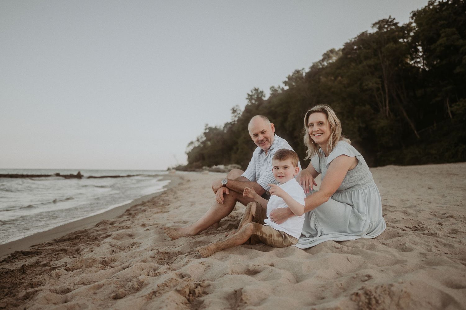 Family sitting together on a sandy beach with forest backdrop during golden hour.