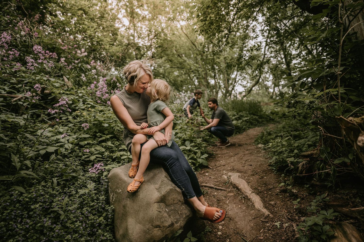 Candid moment of family bonding while sitting on large rock along forest trail.