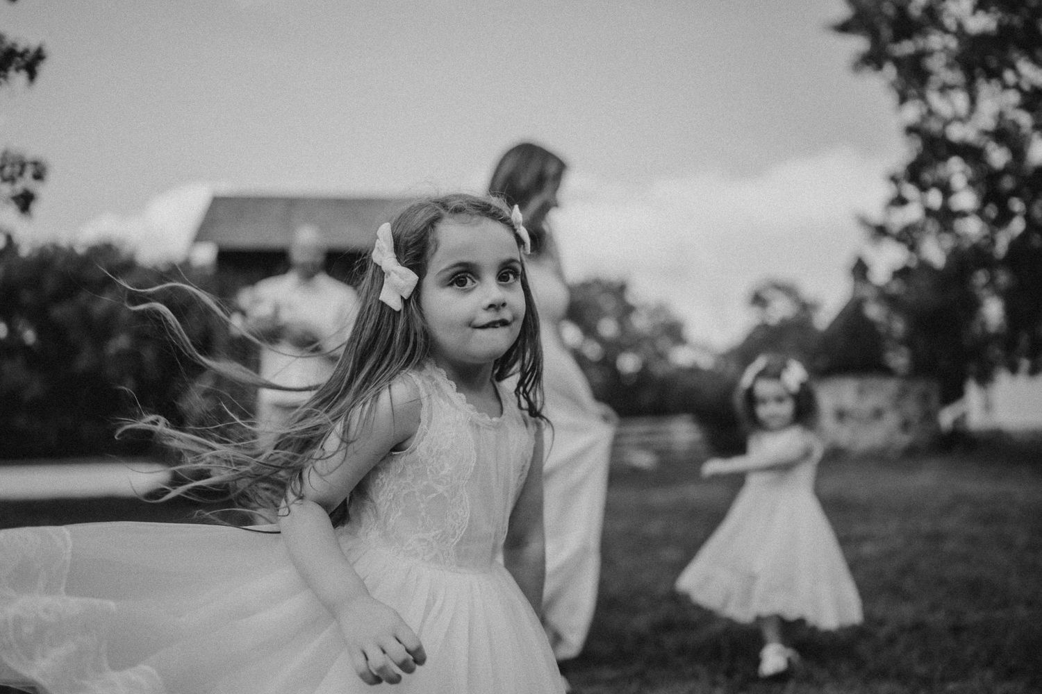 Young girls in white dresses twirling in a sun-lit garden setting.