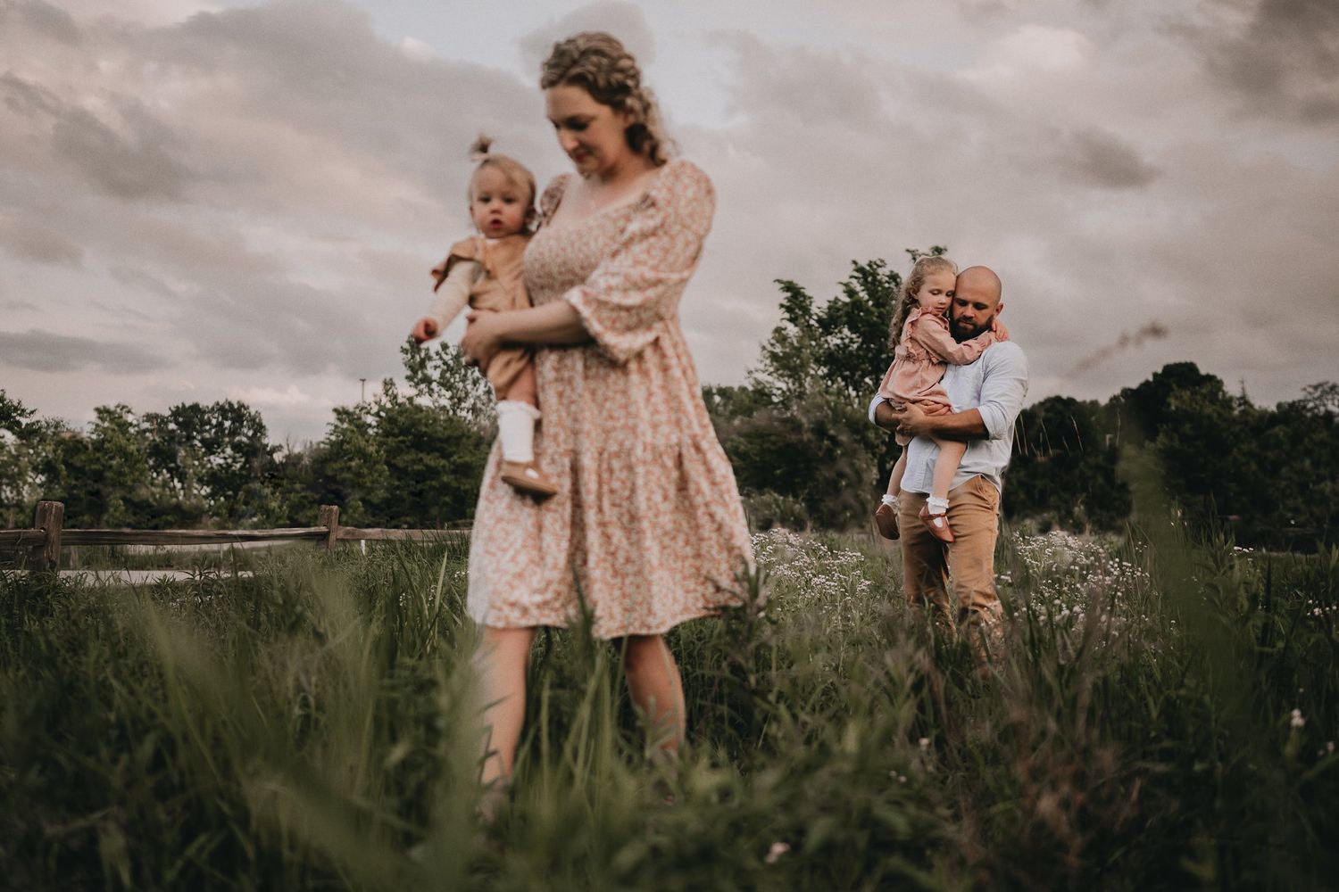 A family enjoys a tender moment together in a rustic field at sunset.