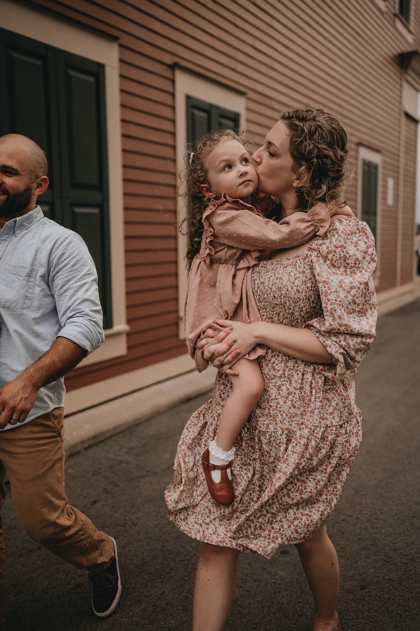 A candid family moment captured on a street with rustic buildings in the background.