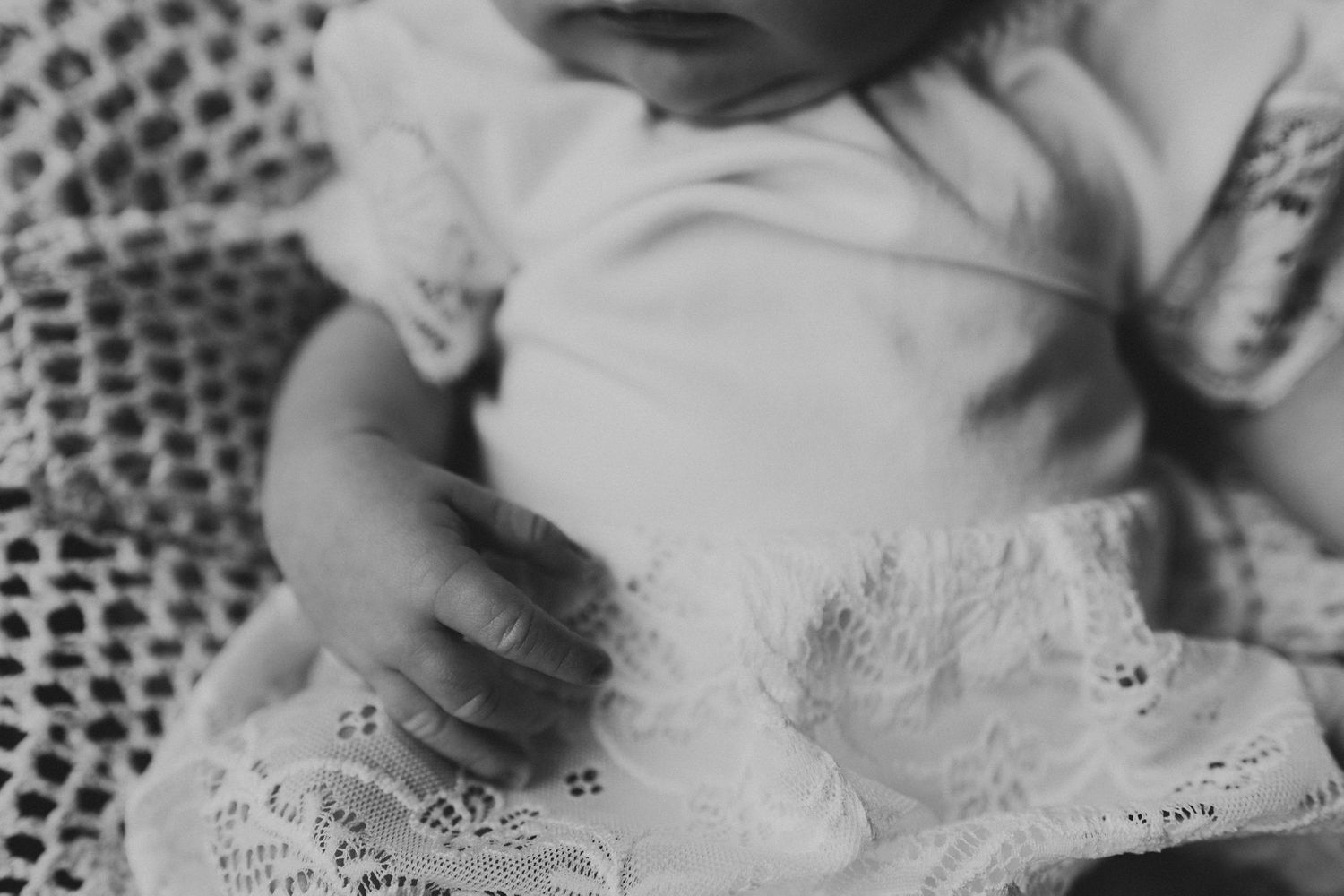 Black and white image of baby hands resting on delicate lace fabric.