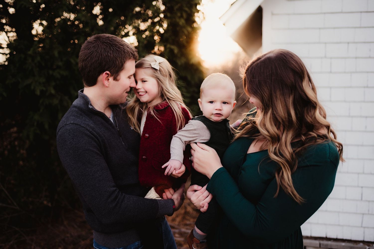 Family portrait with parents and small child outdoors at sunset against white brick wall.