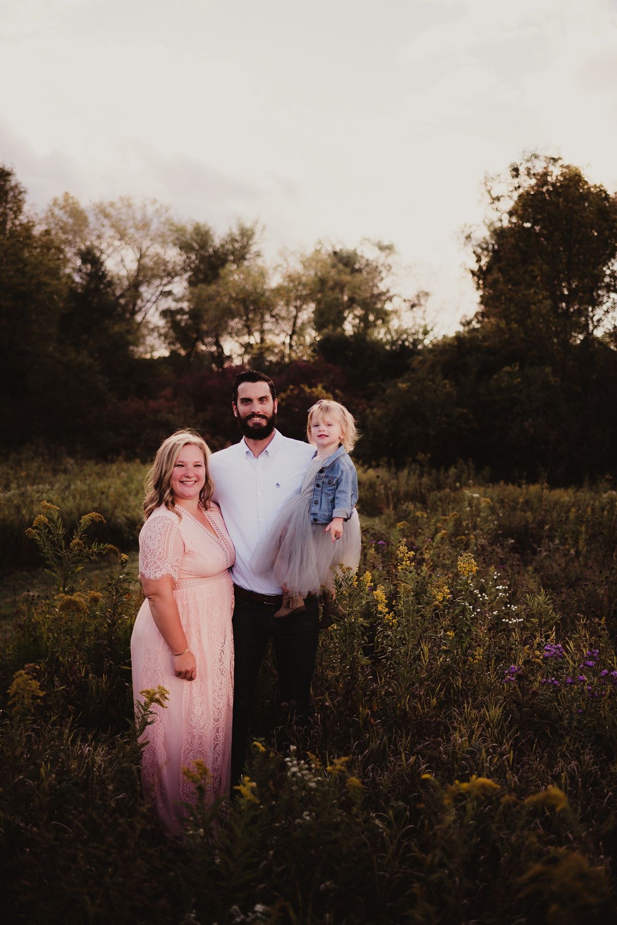 A family portrait taken in a wildflower meadow at sunset with soft golden lighting.