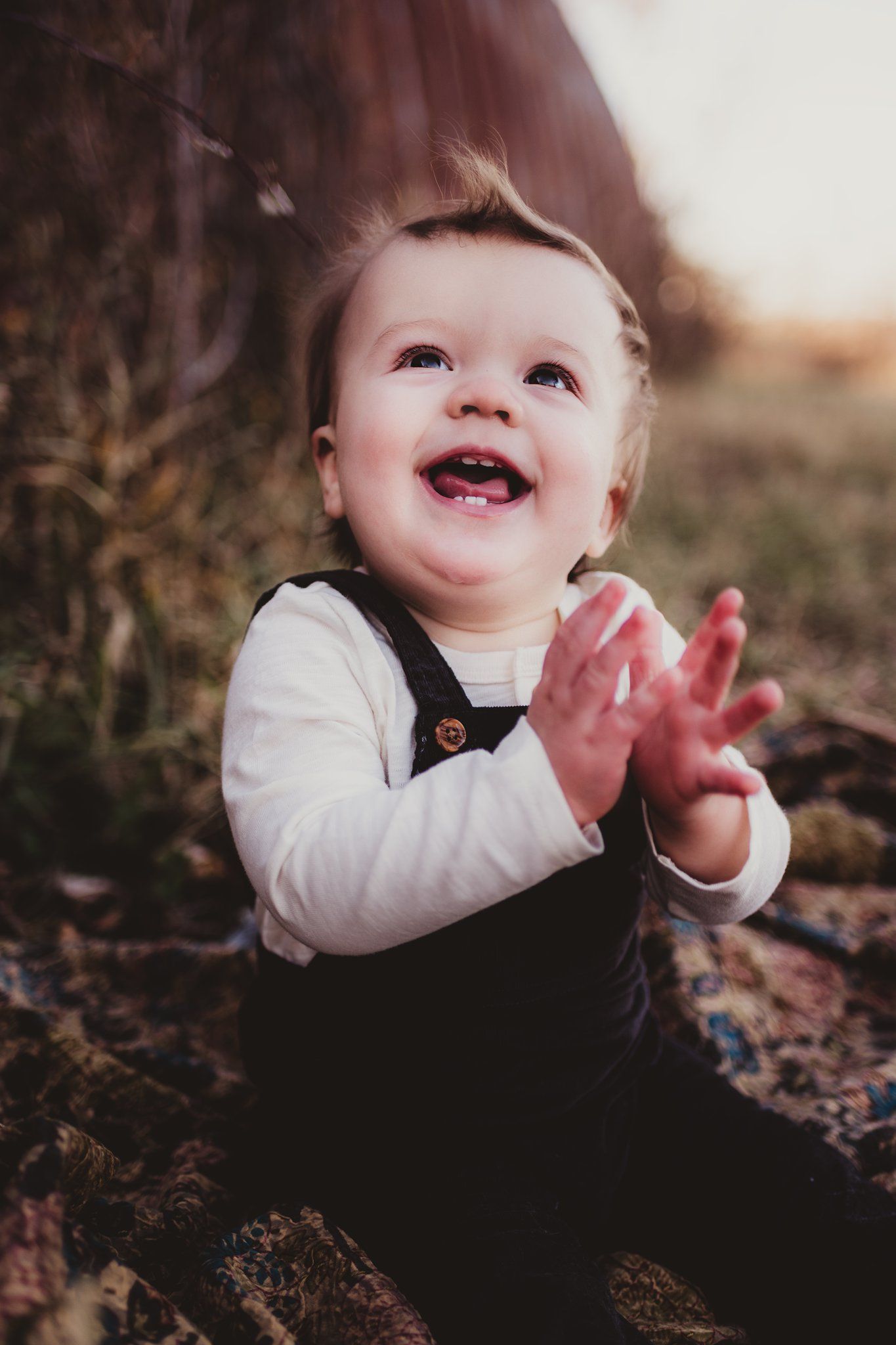 Joyful baby in overalls clapping and laughing outdoors.