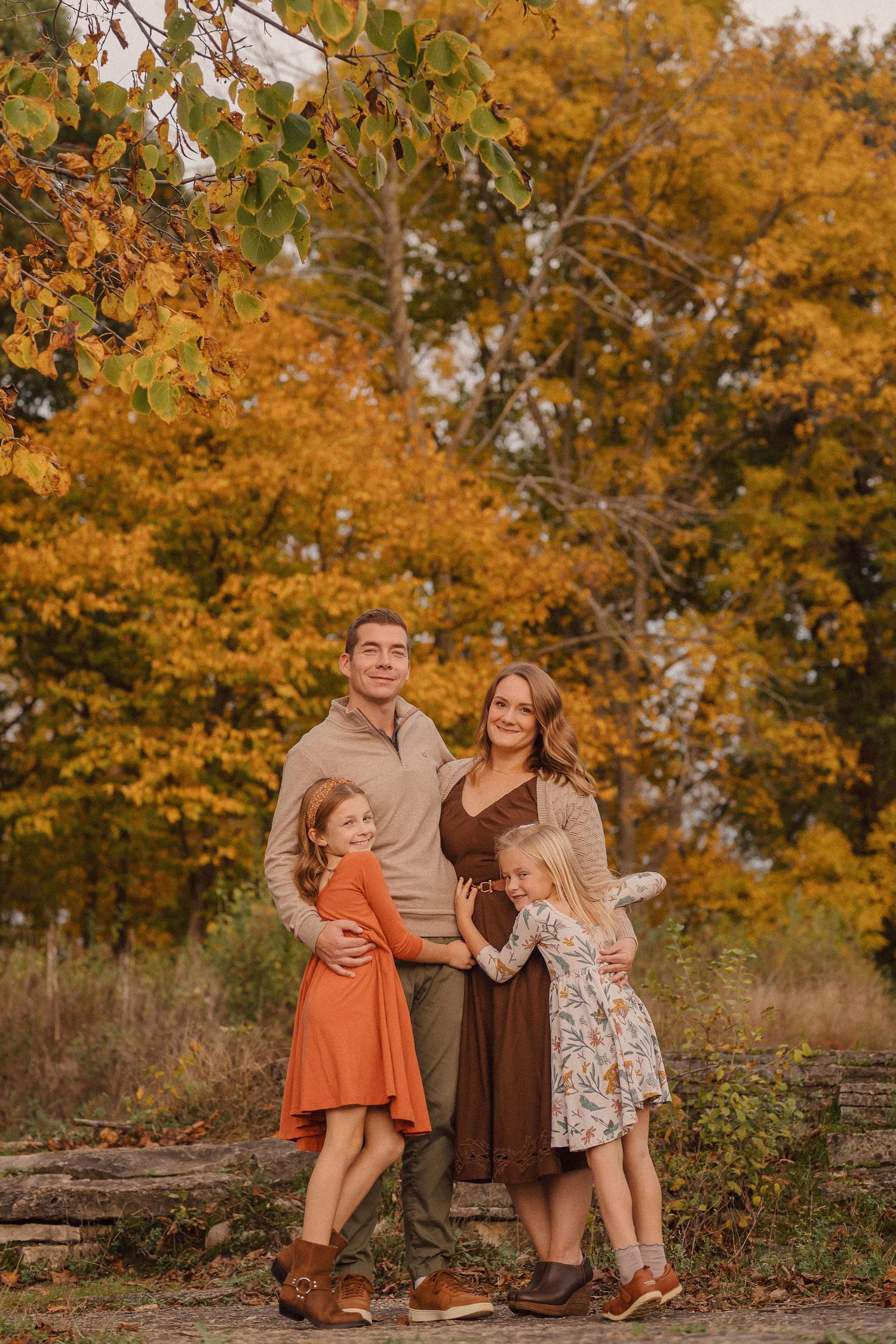 Family portrait on stone steps with beautiful fall foliage in warm golden tones.