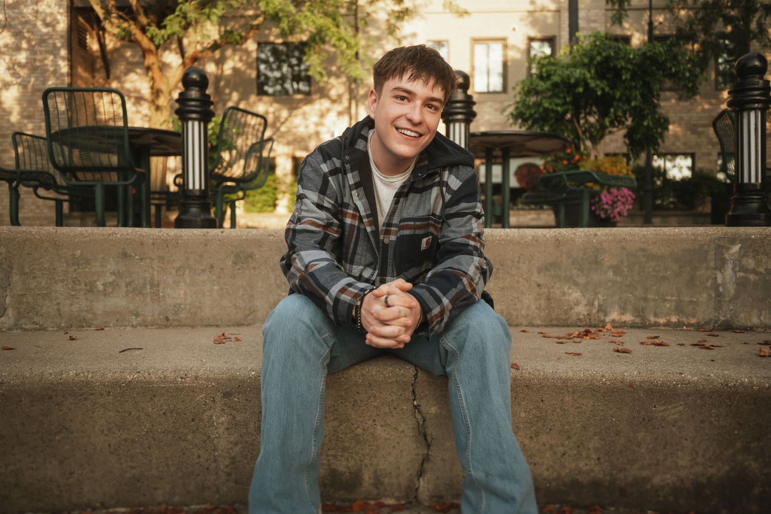 A relaxed portrait of someone sitting on concrete steps wearing casual streetwear and smiling at the camera.