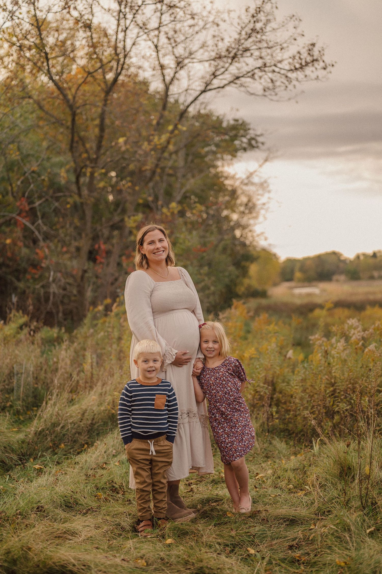 A family stands together in a golden autumn field at sunset with tall grass and trees in the background.