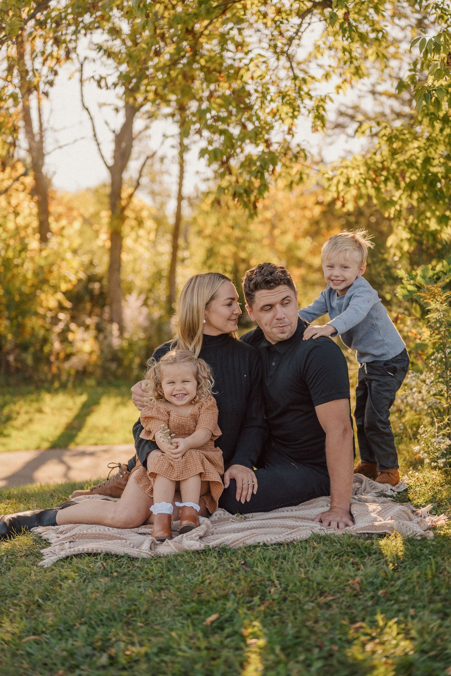 Candid family moment captured during outdoor photoshoot on grassy hill with autumn trees.