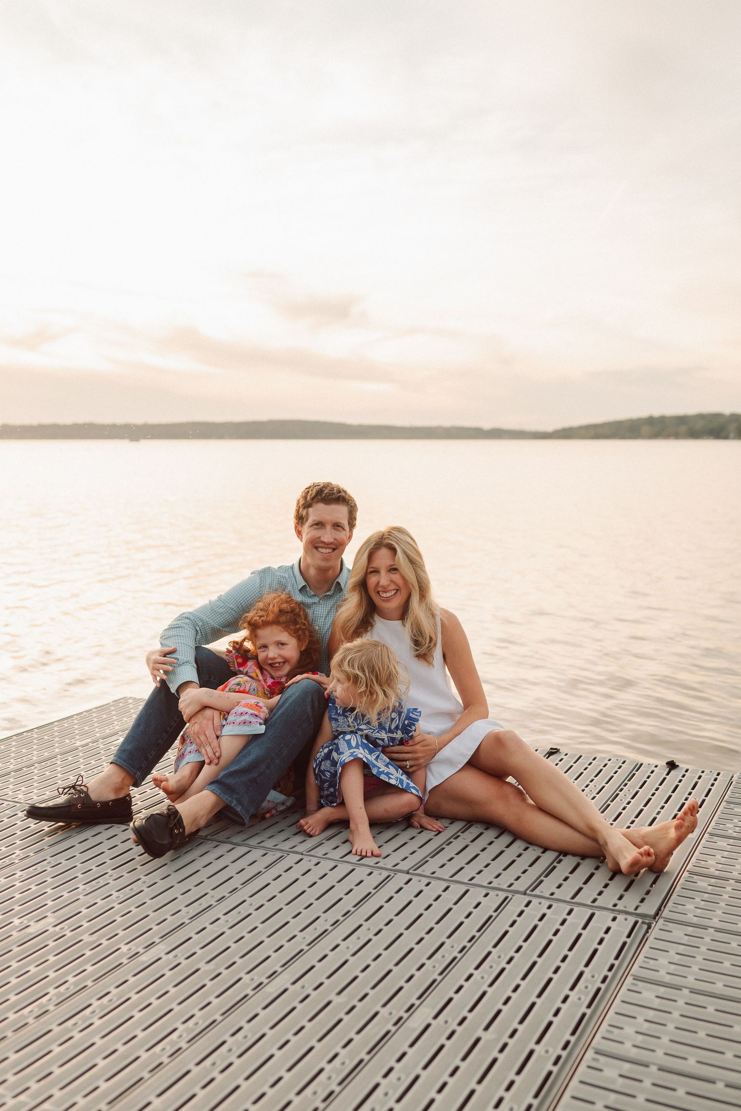 A joyful group shares laughter while lounging on a lakeside dock at dusk.