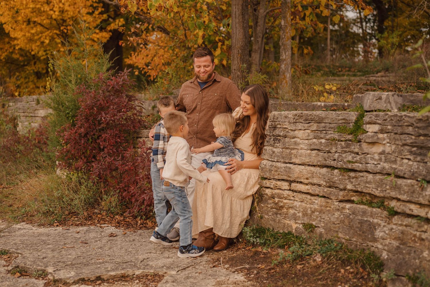 A couple sits together on stone steps surrounded by autumn foliage in a romantic outdoor setting.