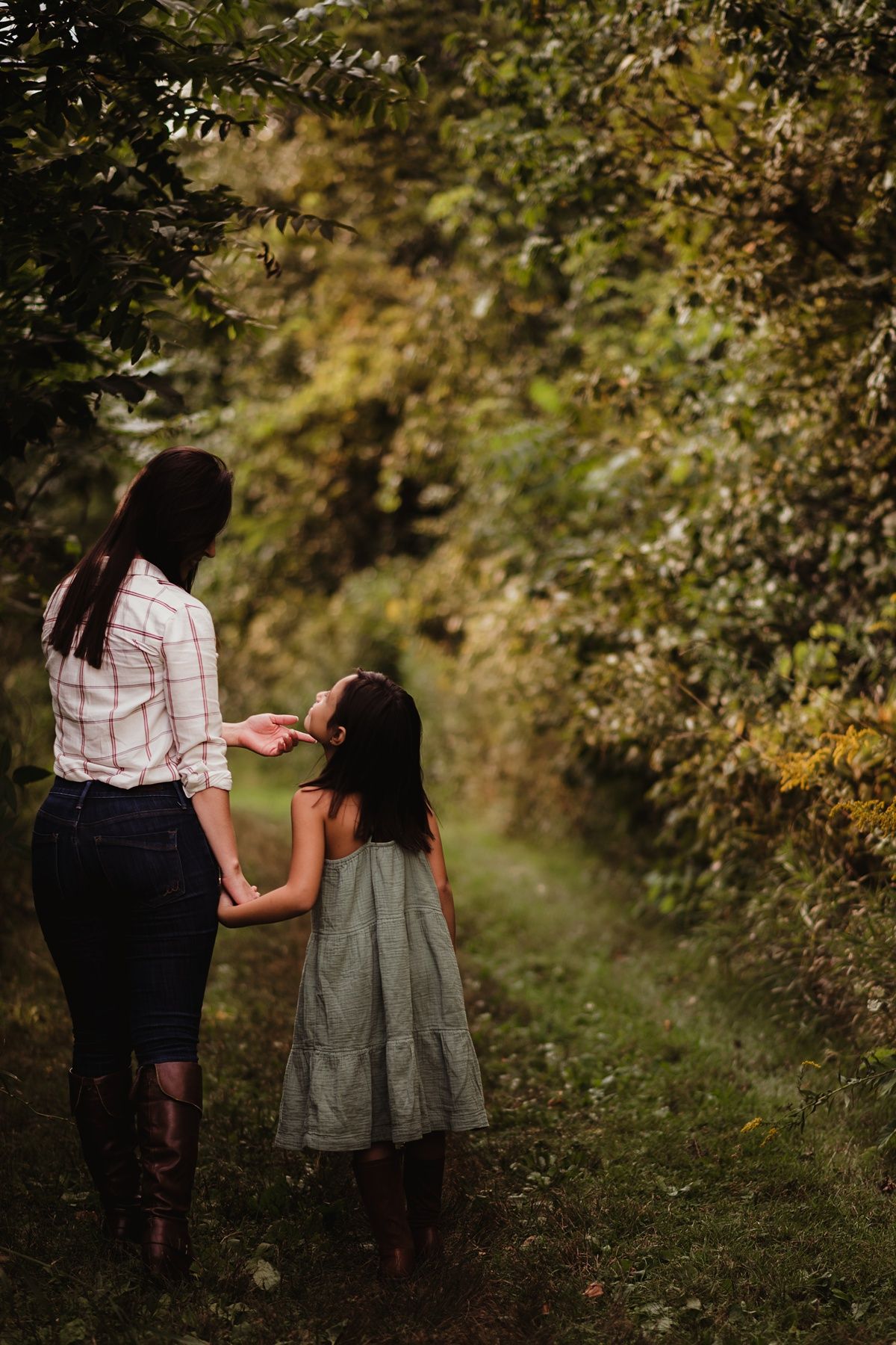 Mother and daughter walking hand in hand down a nature path during sunset.