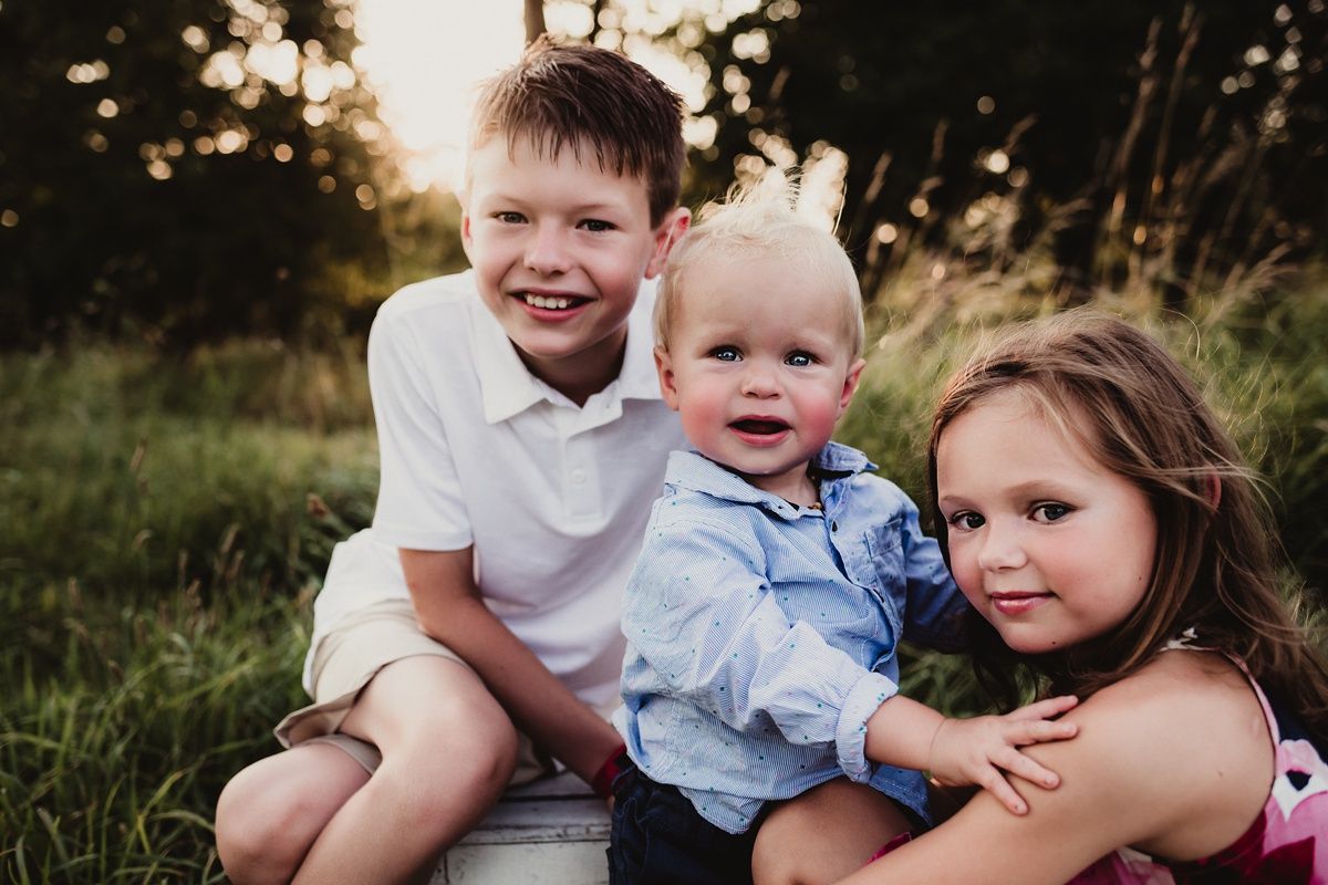 Three children sit close together on grass during an outdoor photo session.