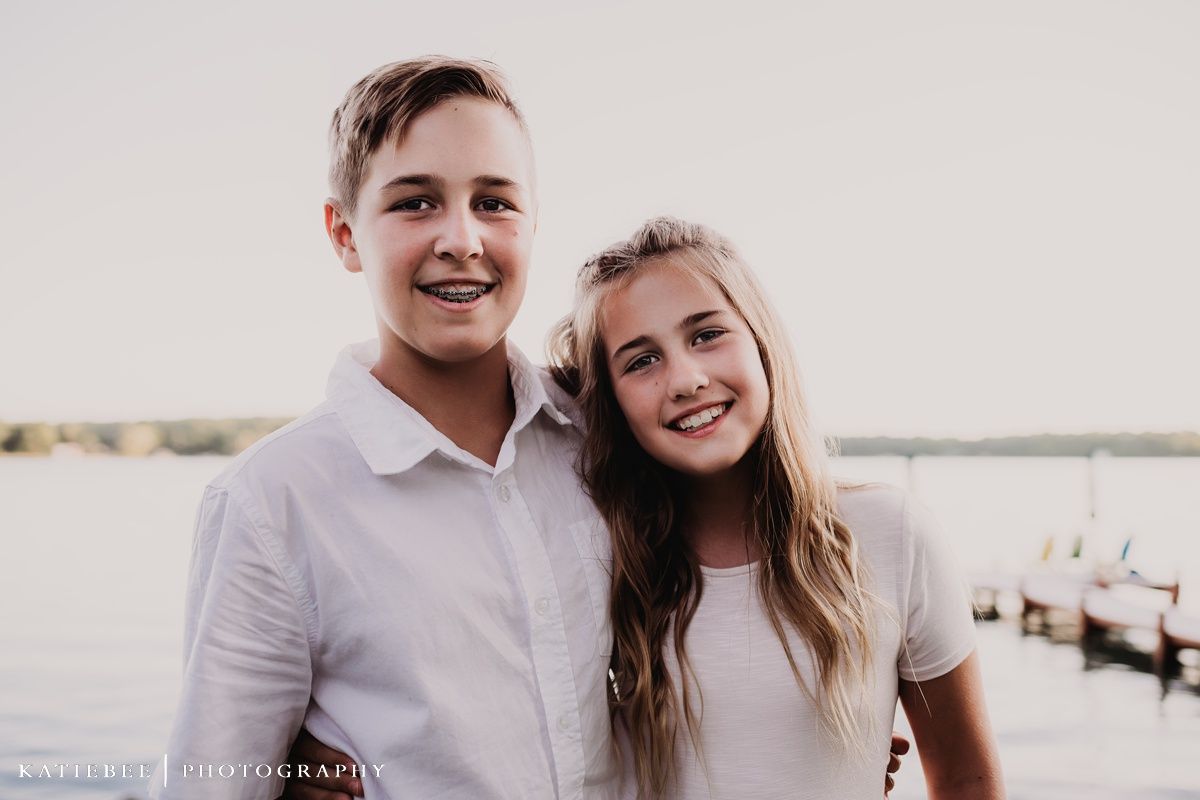 Young pair in light colored clothing smiling together against lakeside background.