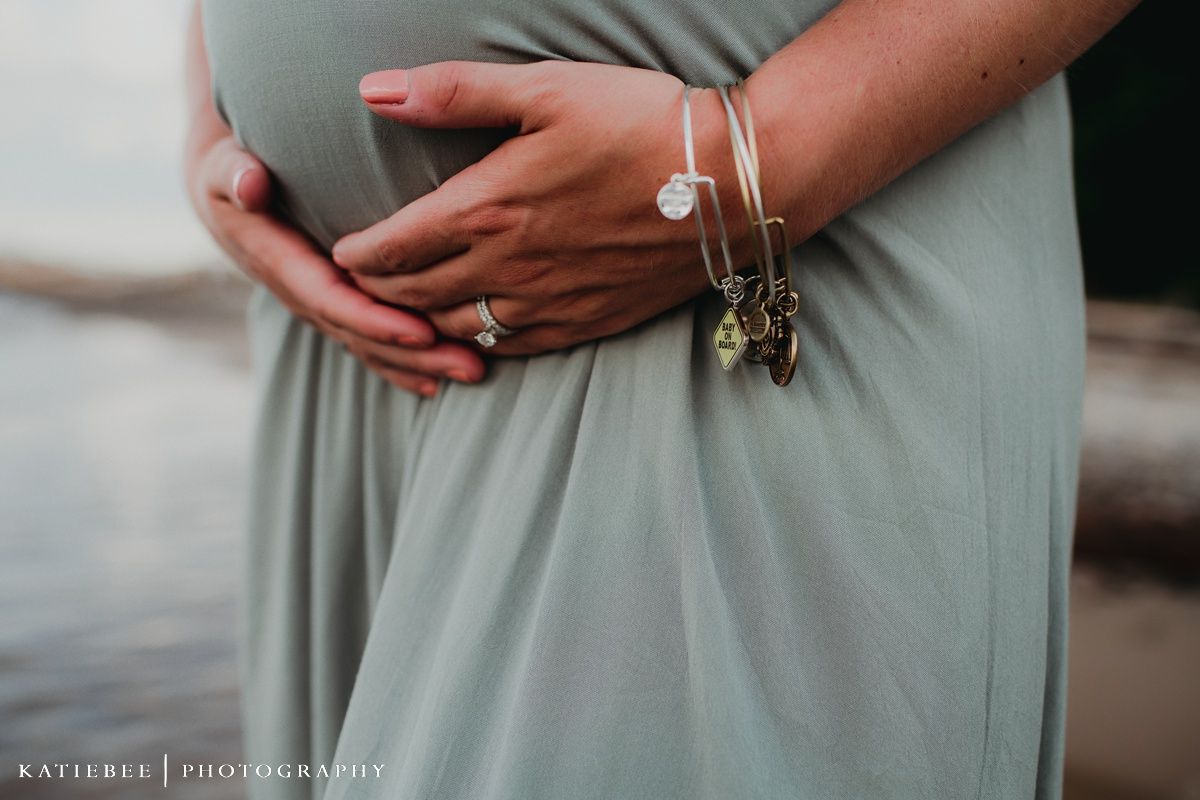 Close-up of hands resting on pregnant belly with delicate bracelets.