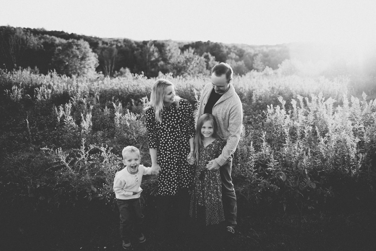Black and white portrait of family standing together in wildflower field at dusk.