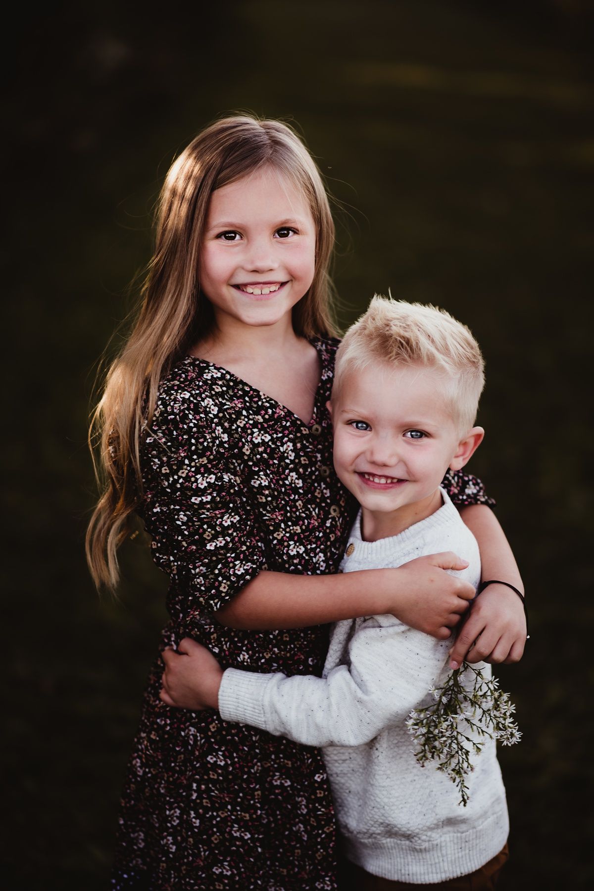 Siblings in coordinating outfits embrace while smiling for a portrait outdoors.