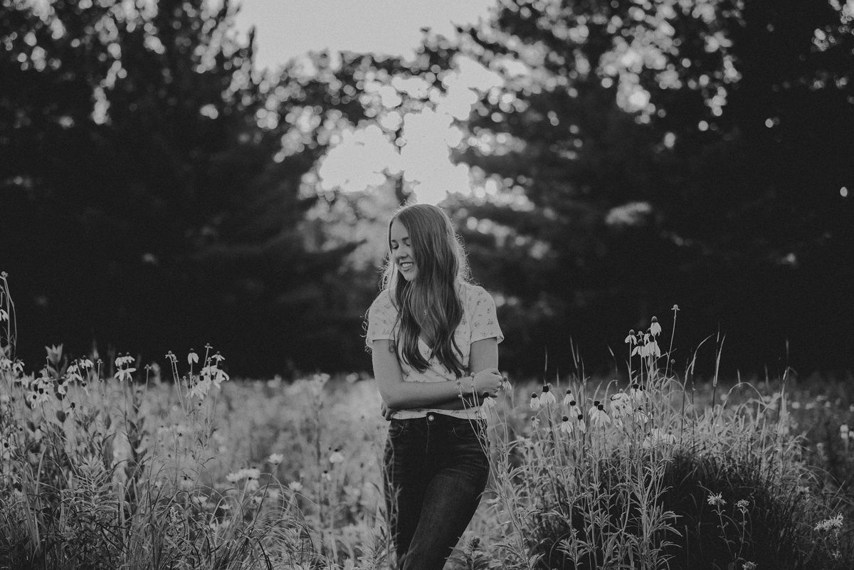 Black and white portrait in a meadow with tall grass and evergreen trees in background.