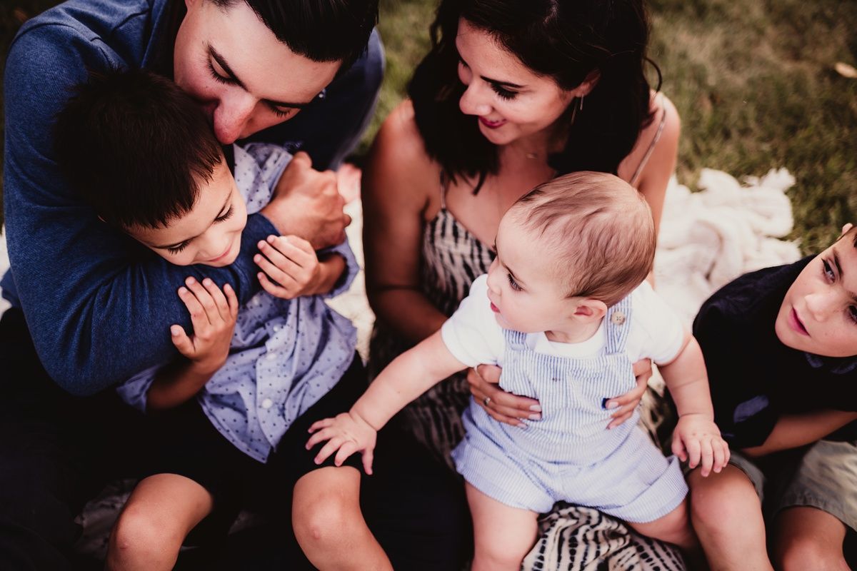 Family sitting close together on blanket during outdoor photo session.