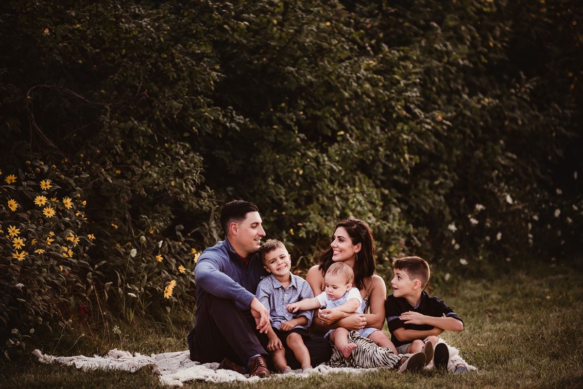 Family relaxing on blanket during sunset photo session with autumn leaves in background.