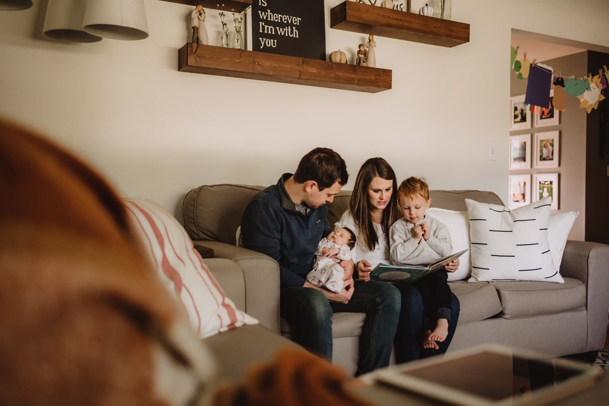 Intimate family moment on couch with baby and book in modern living room.