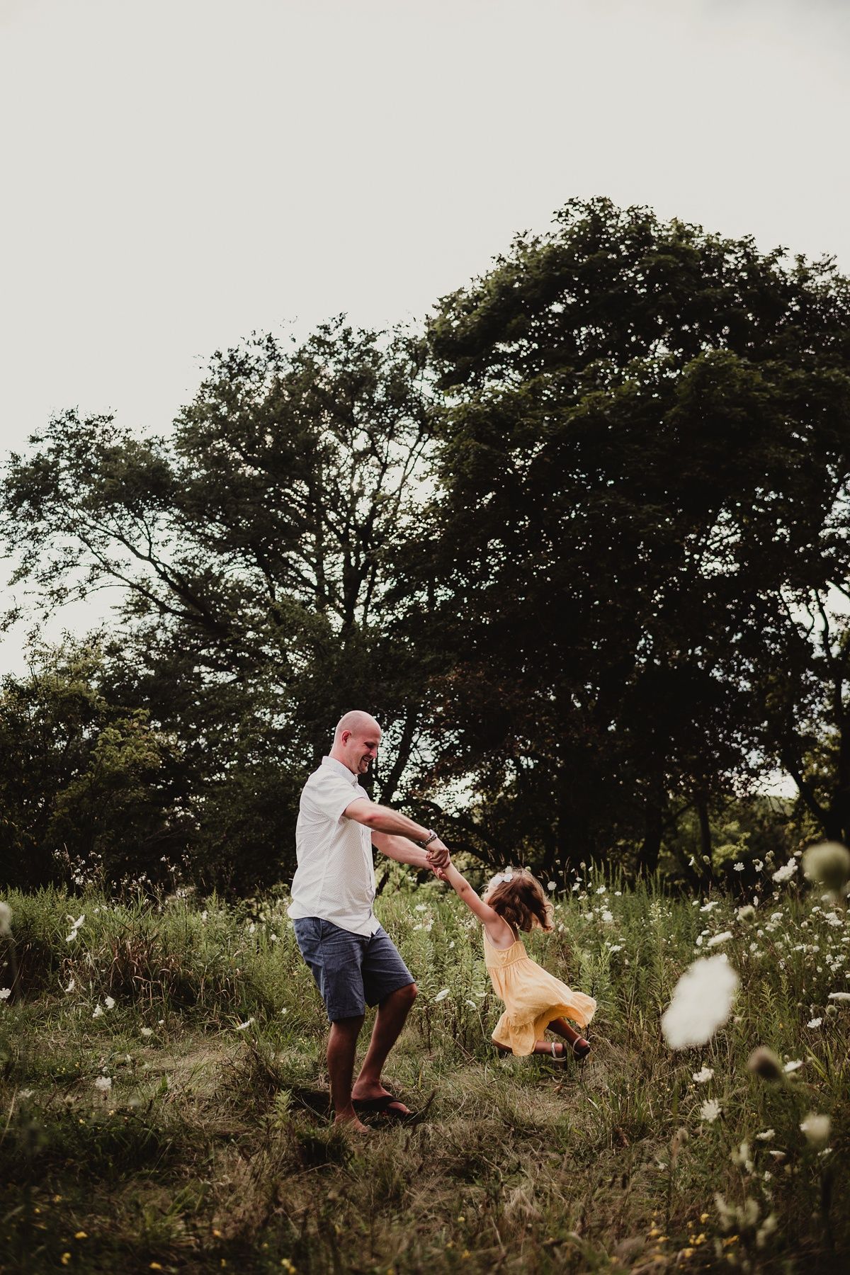 Parent and child playing and spinning in a field during golden hour.