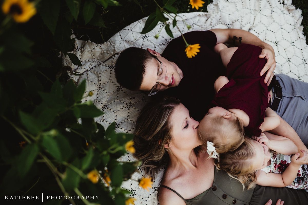 Overhead view of family lying on white blanket surrounded by sunflowers.