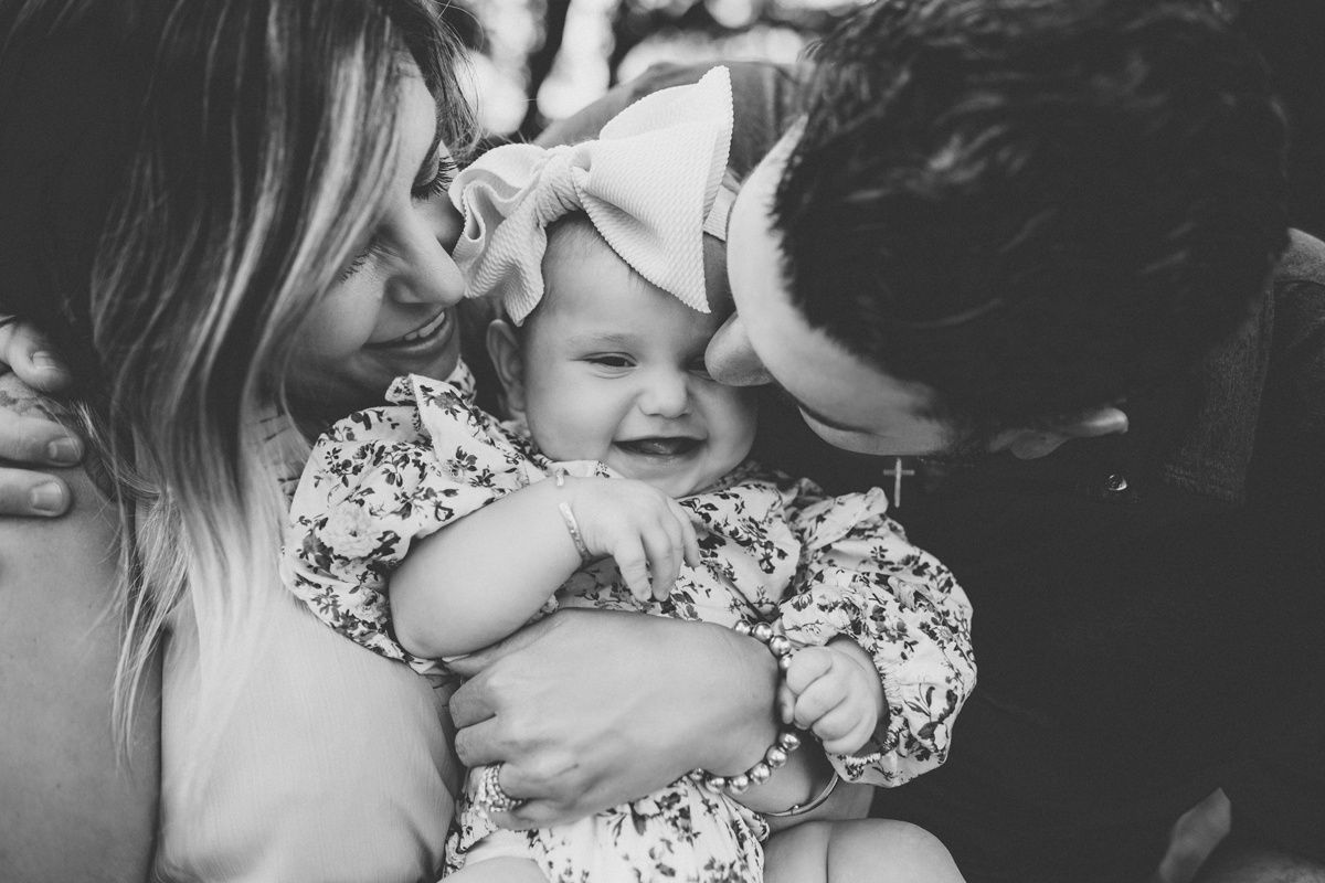 A tender black and white family moment showing parents sharing joyful affection with their baby.
