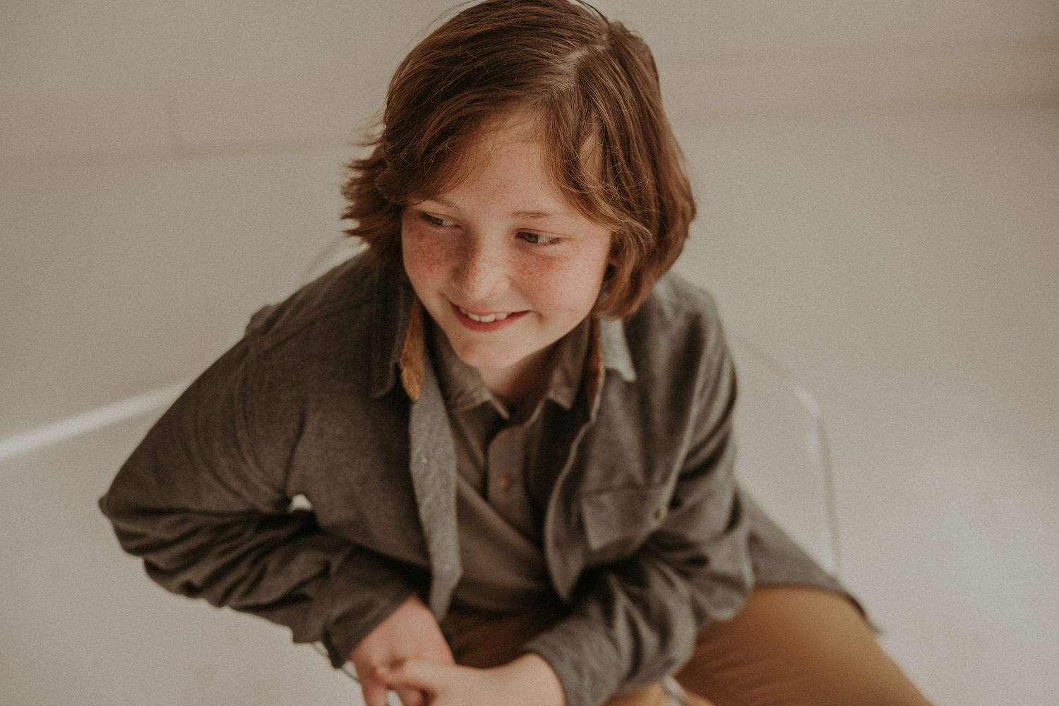A candid portrait showing someone in brown attire seated comfortably in a white chair.