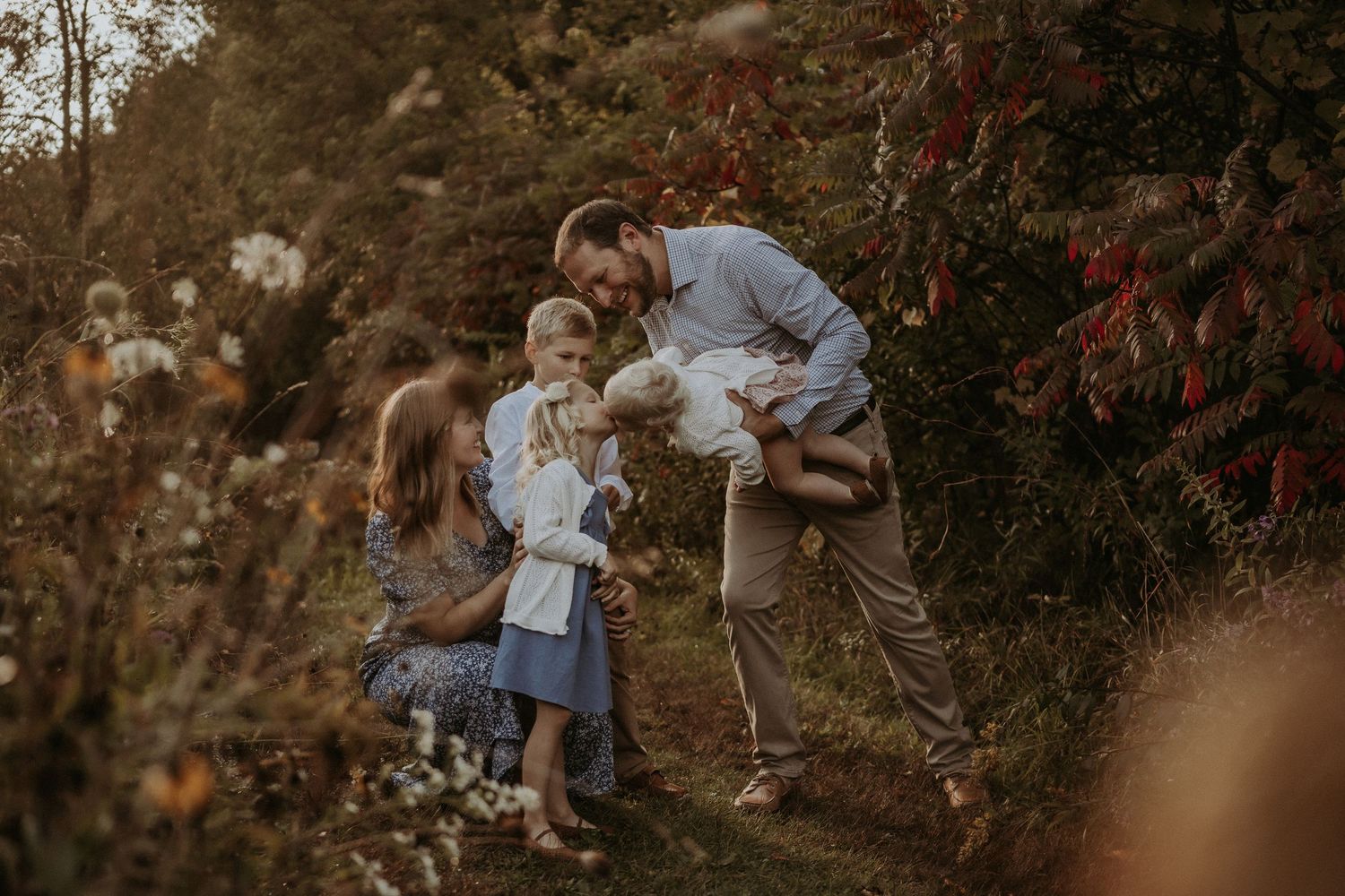 Family enjoying a playful moment together on a wooded hillside during golden hour.