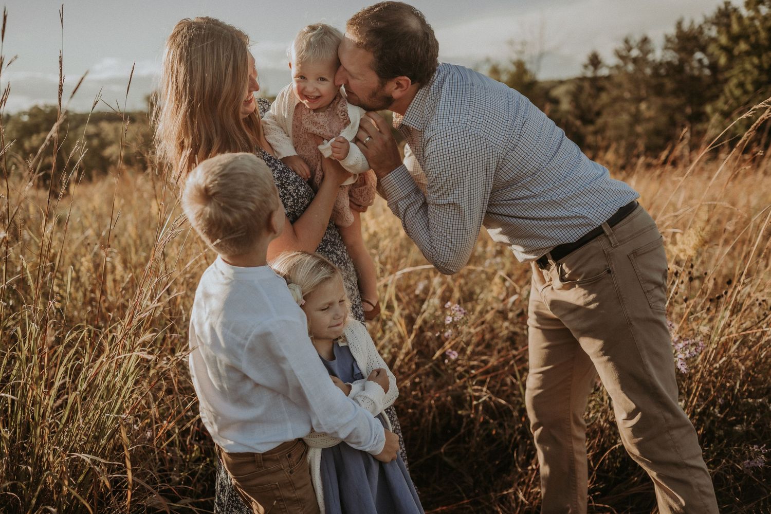 Candid family interaction captured in golden meadow during sunset photoshoot.