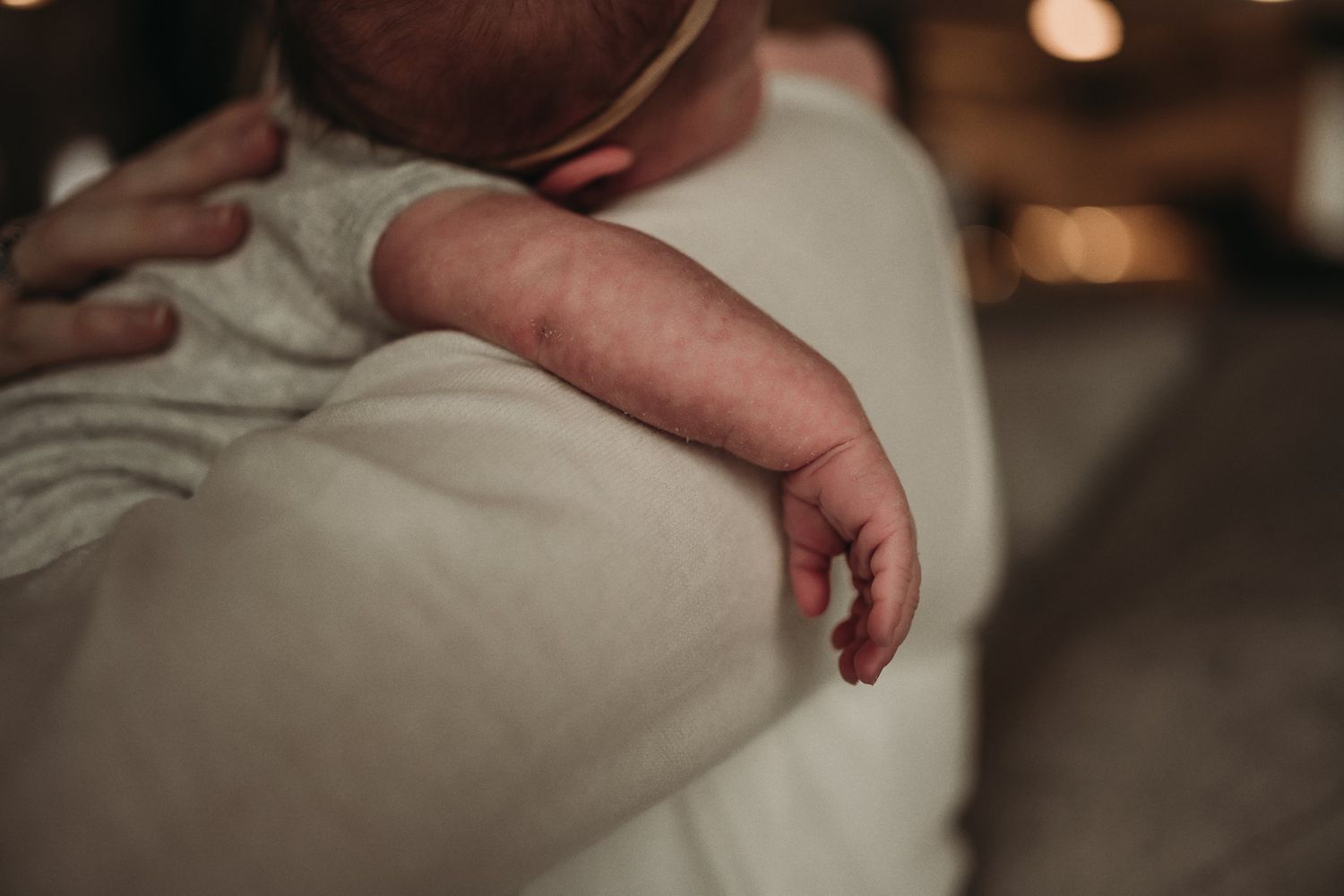 Close-up of tiny newborn's hand resting against white clothing.