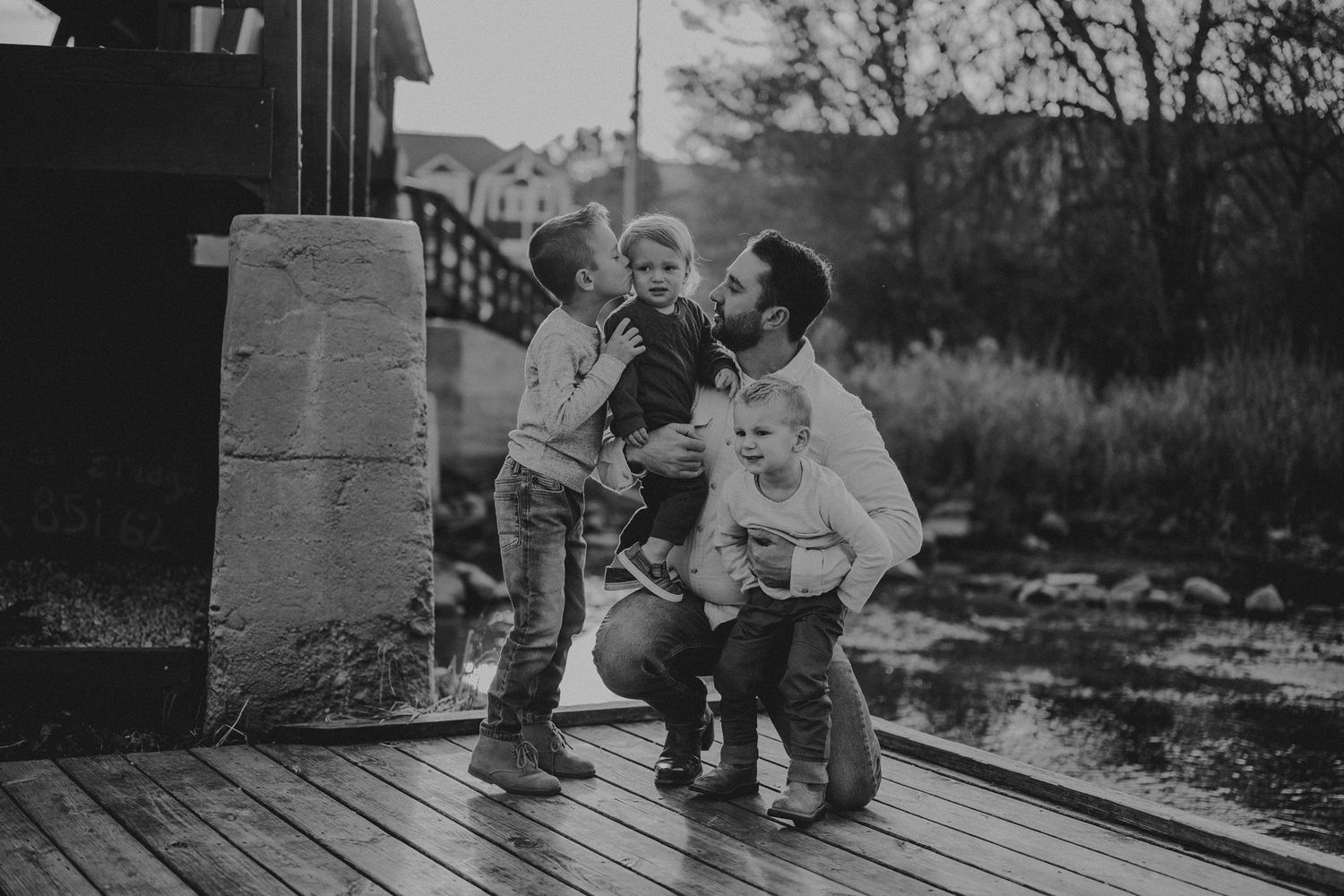 A black and white capture of playful family interactions on a rustic wooden deck.