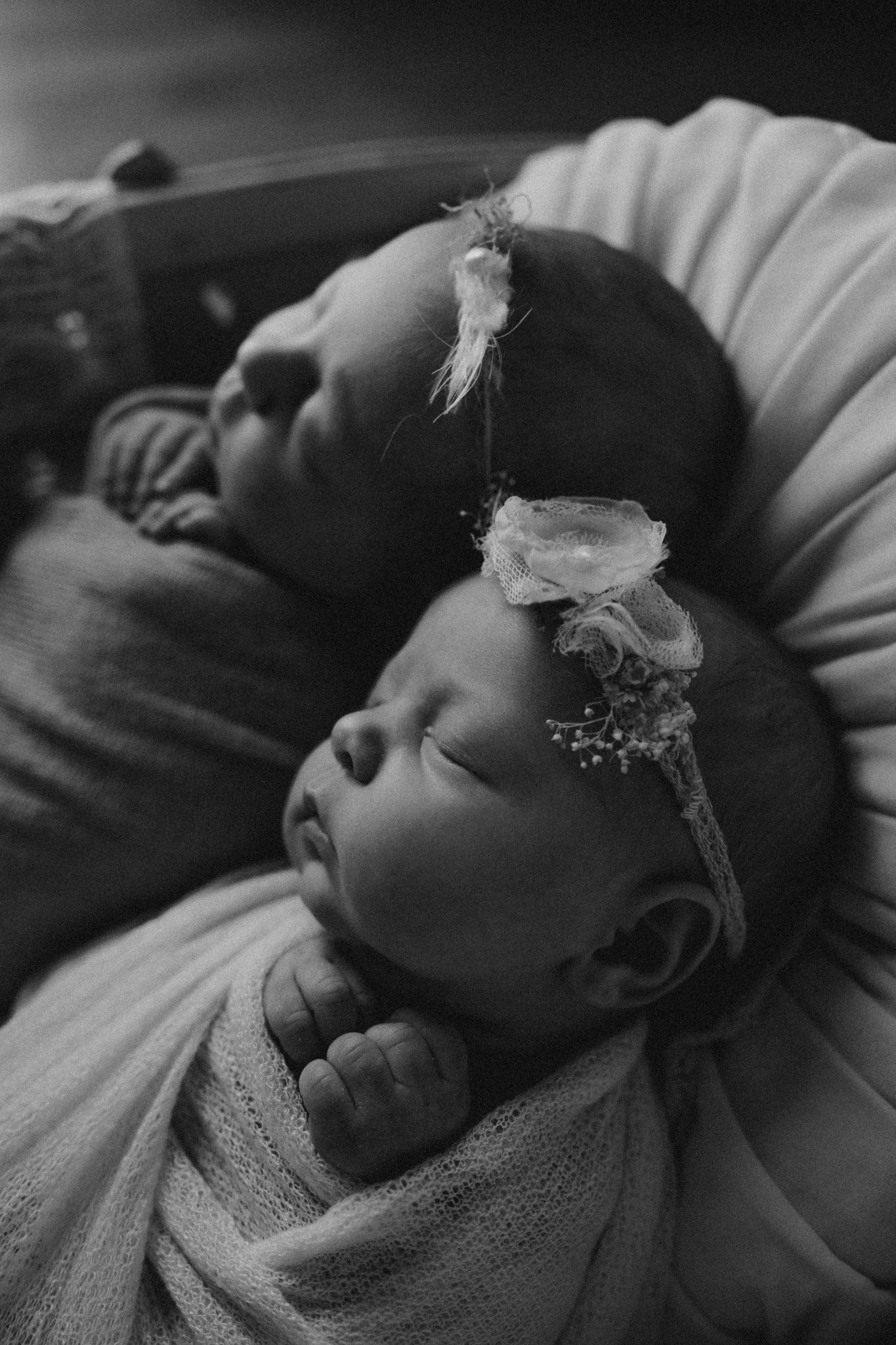 Black and white close-up of twin infants sleeping with lace headbands.