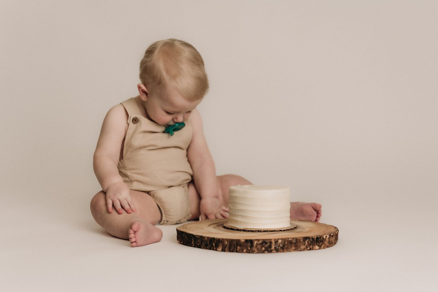 White frosted cake displayed on rustic wood slice with greenery.