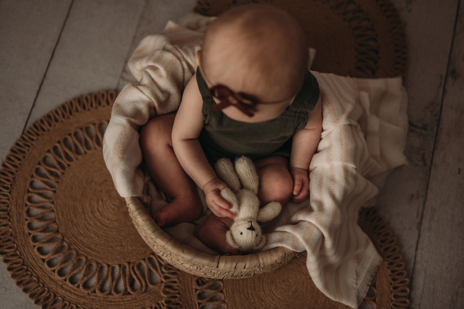 Overhead view of baby in dark outfit sitting in woven basket.