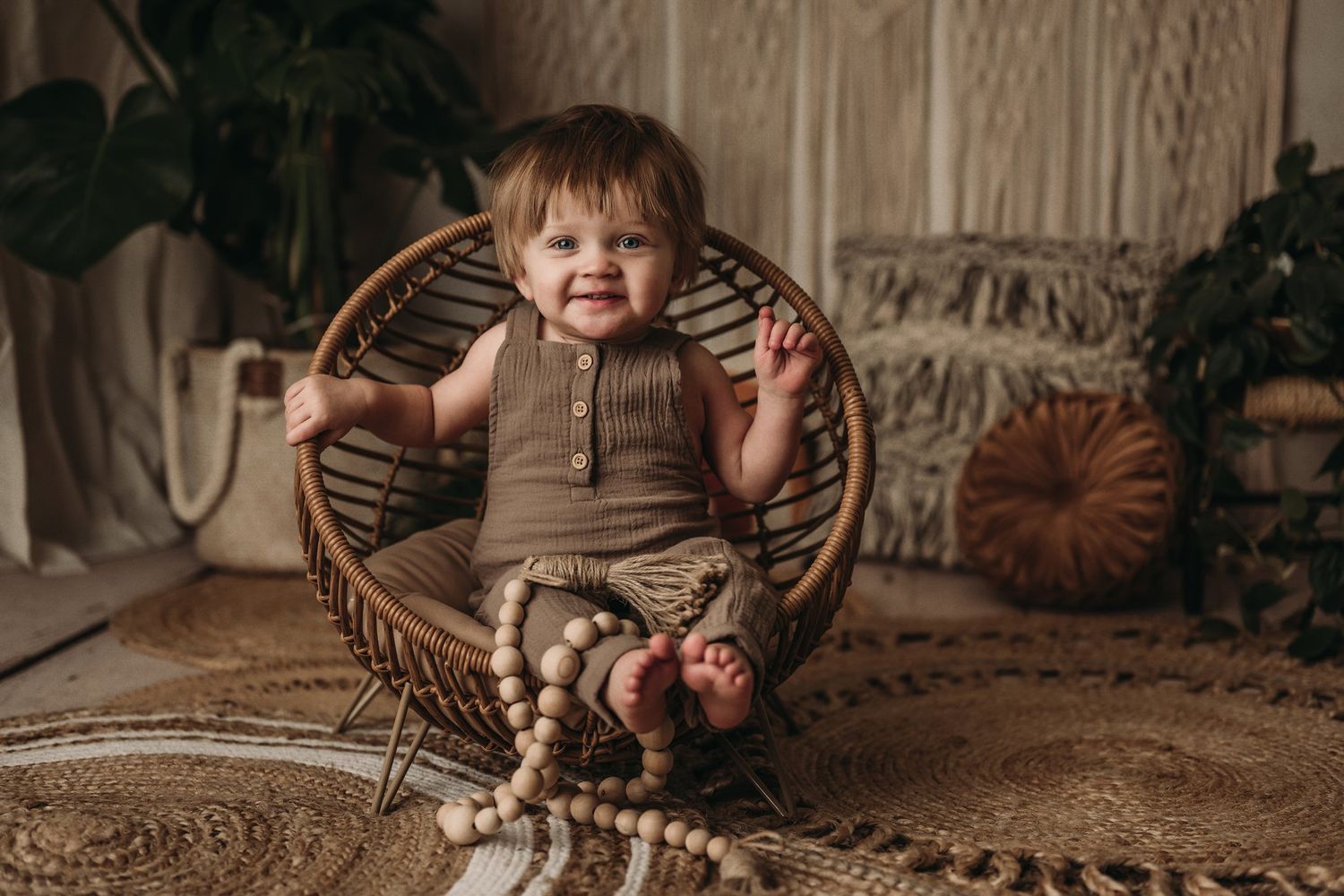 A joyful toddler sits in a wicker papasan chair with decorative wooden beads nearby.