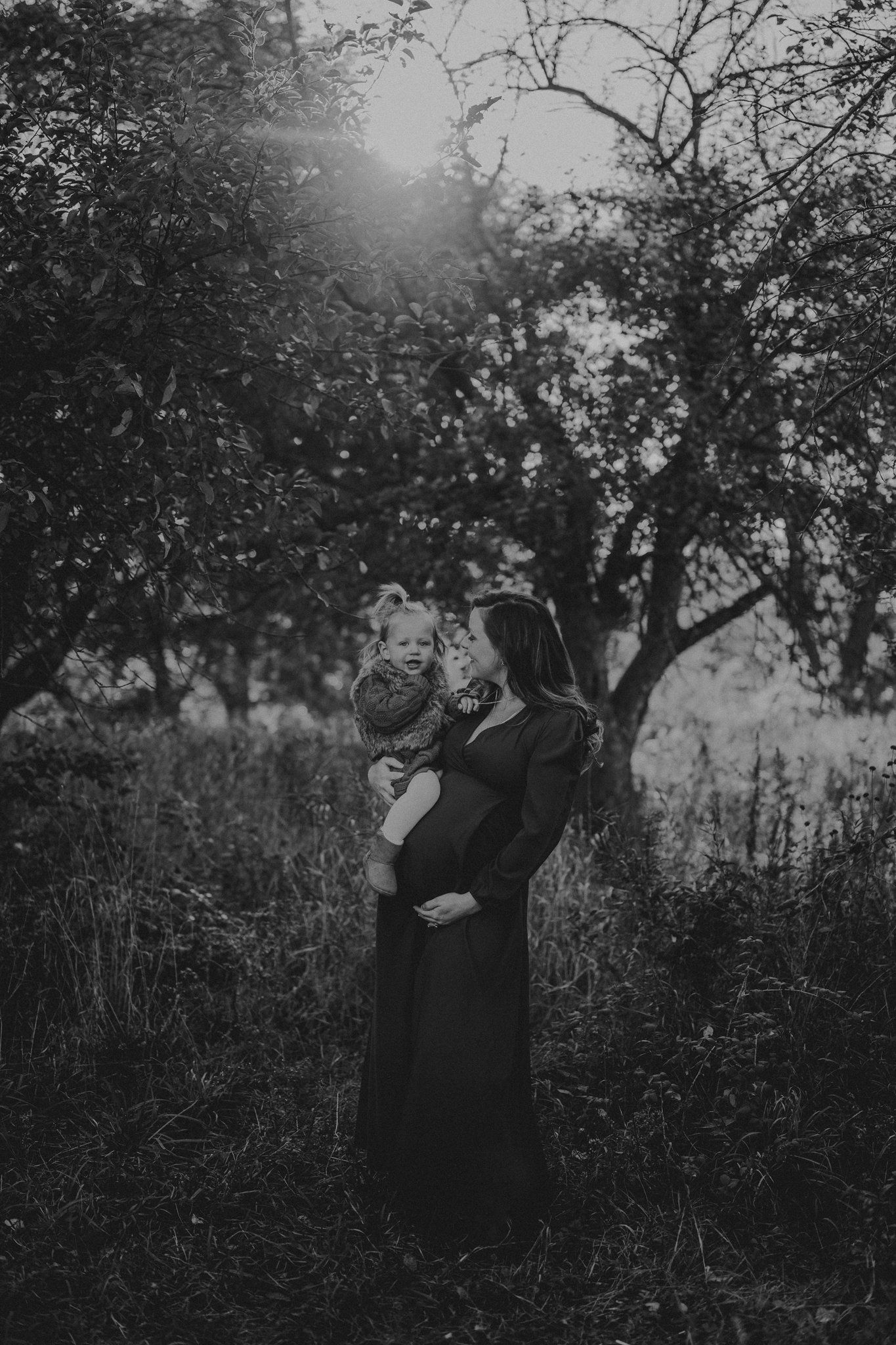 Black and white portrait showing a gentle embrace among trees at dusk.