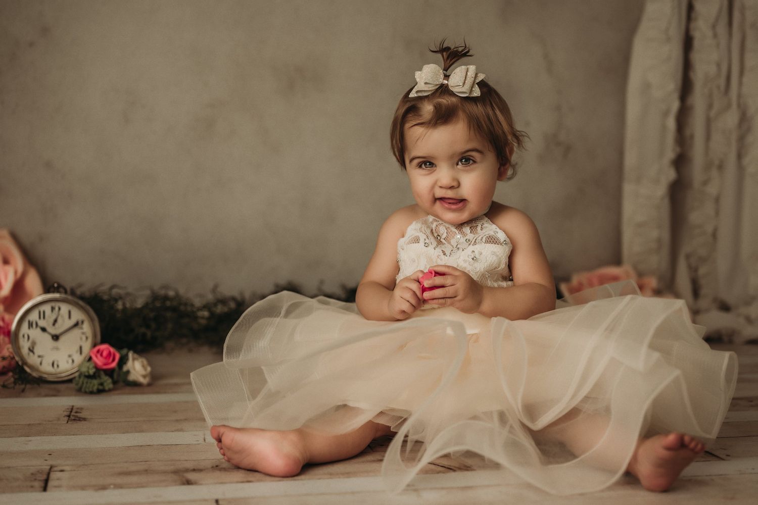 An elegant portrait setup with vintage clock and roses features a cream tulle dress against neutral background.