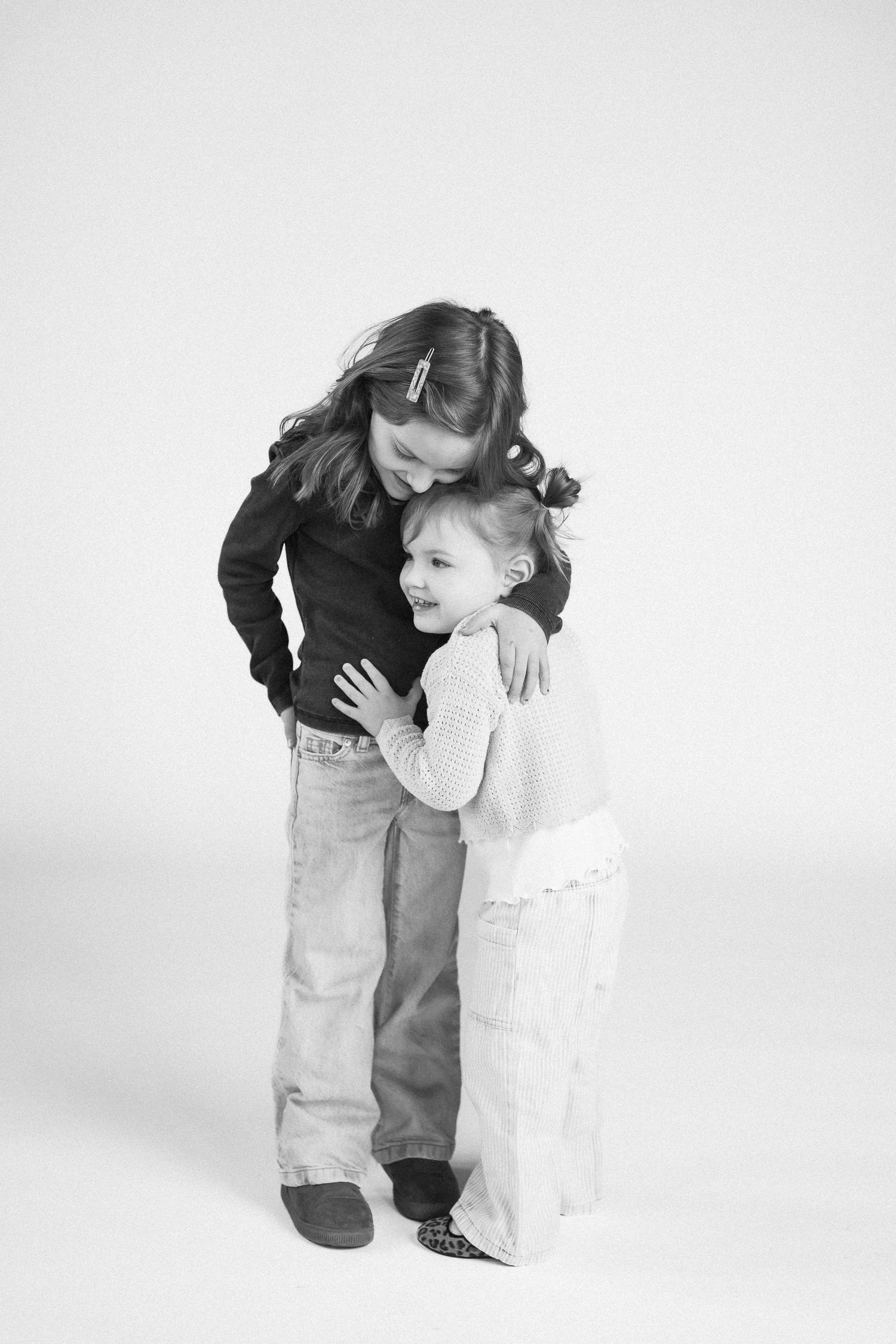 Black and white portrait series showing tender embraces between parent and child in minimalist studio setting.