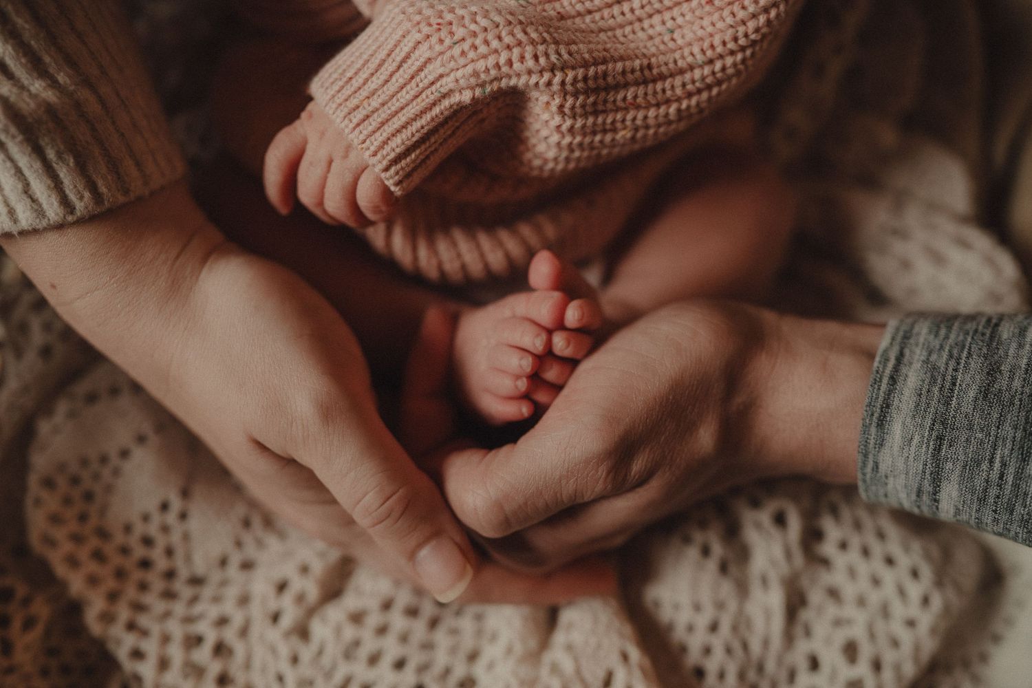 Gentle hands holding and caressing small baby feet against knitted blanket background.